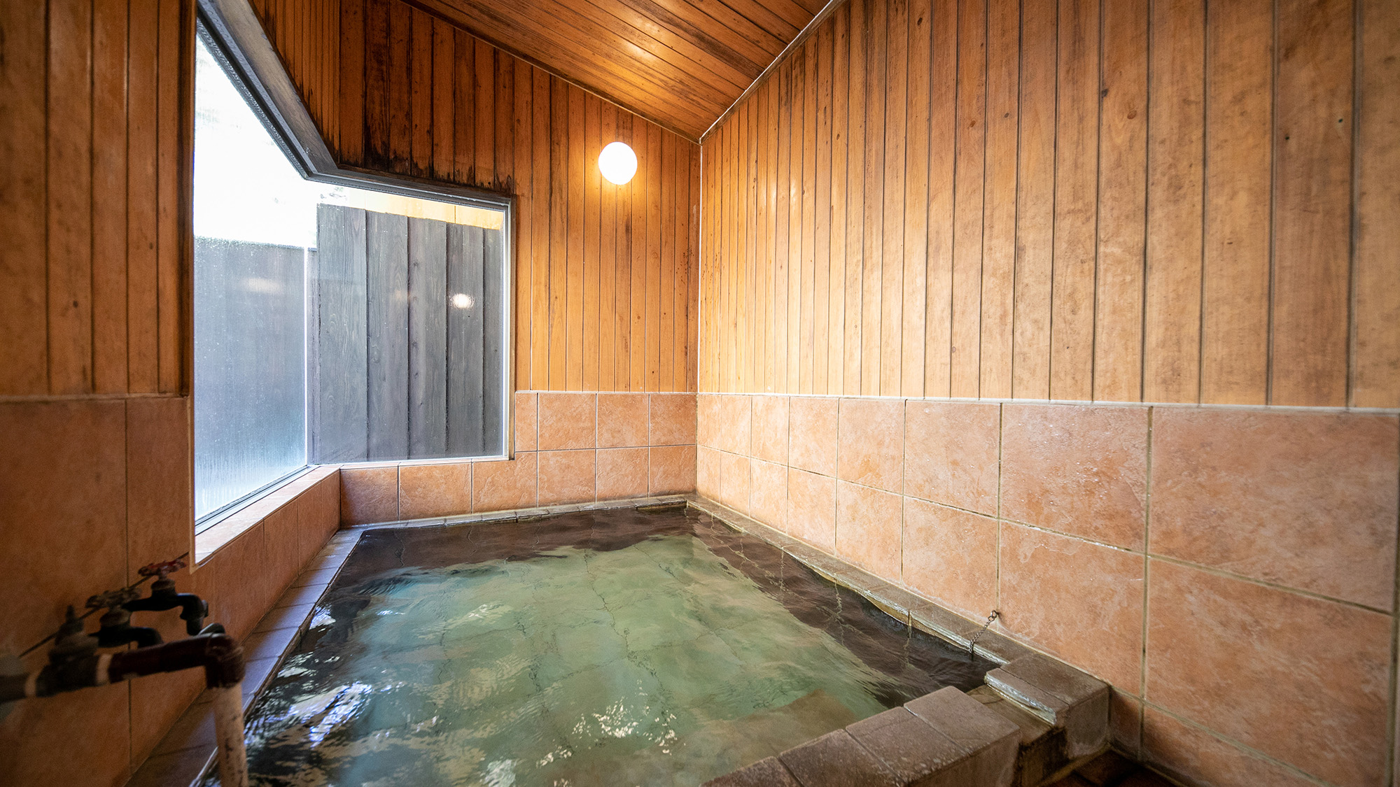 【内湯】窓の大きく、光彩差し込む明るい室内の温泉。木のぬくもりを感じる空間でのんびりと。