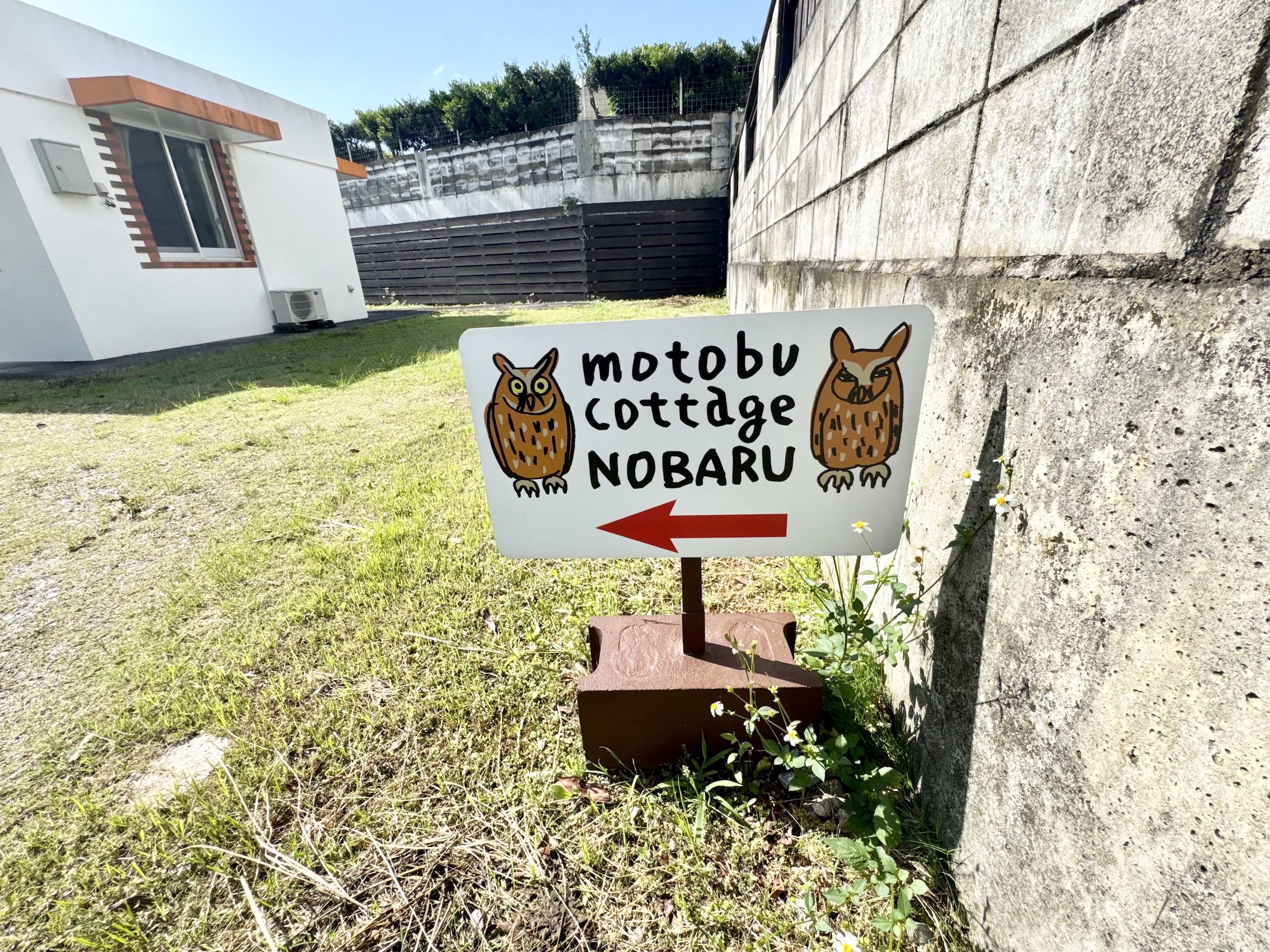 「motobu cottage NOBARU」の文字とフクロウが目を引く看板。住宅街でもパッと目に入り、スムーズな到着をサポートします。