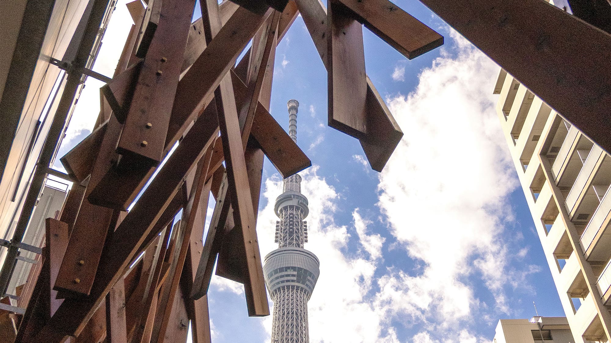 ホテルエントランス（昼）｜木組みのアーチ越しに仰ぎ見る、青空にそびえ立つ東京スカイツリー。