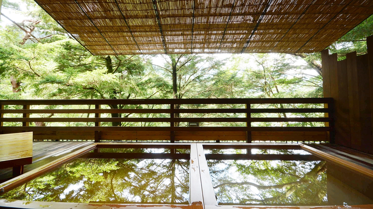 ホテル万葉亭の本館の露天風呂。すだれの屋根の下の湯船の先に、緑の木々が広がる