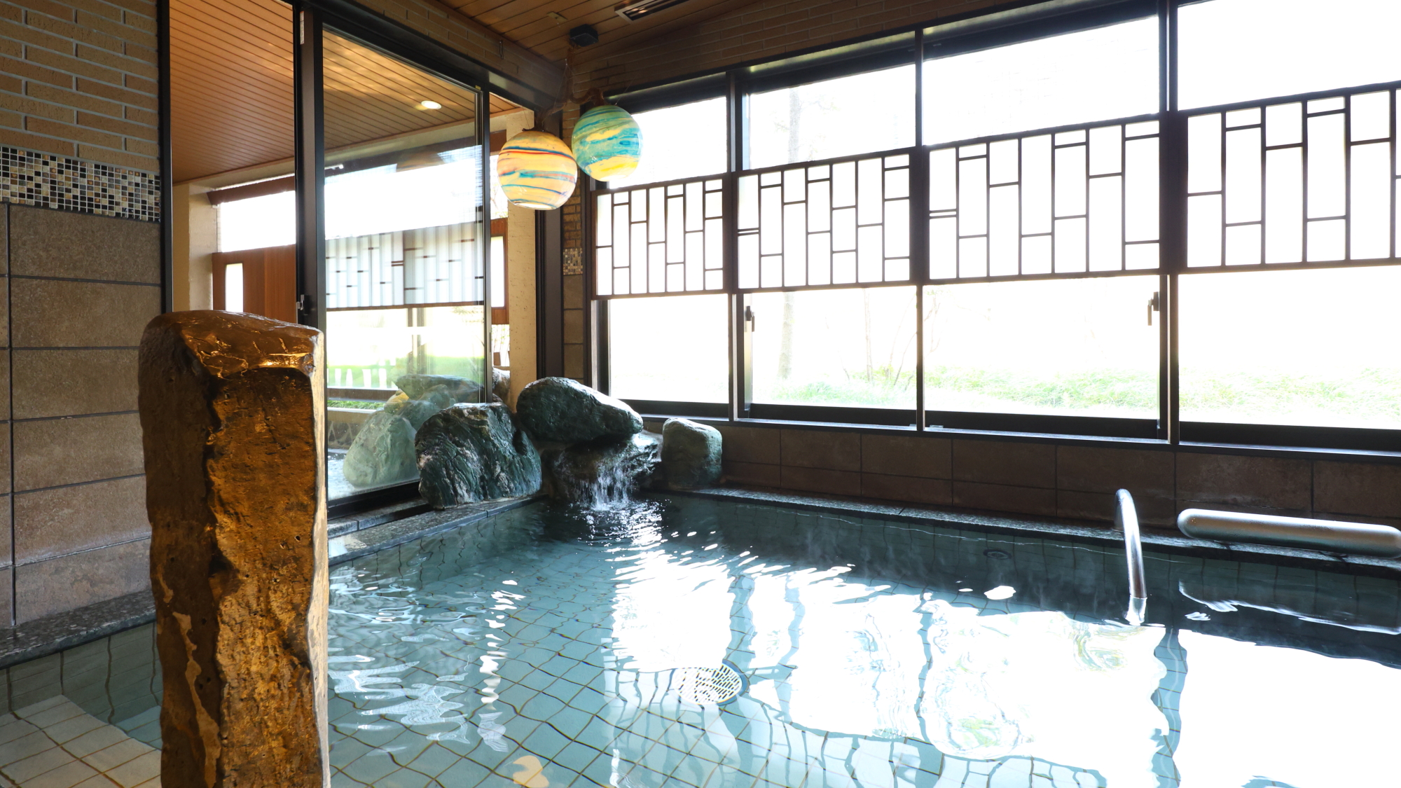 ドーミーインPREMIUM大阪北浜の男性の内湯。石組みから湯が注ぎ、天井から丸い照明が下がっている