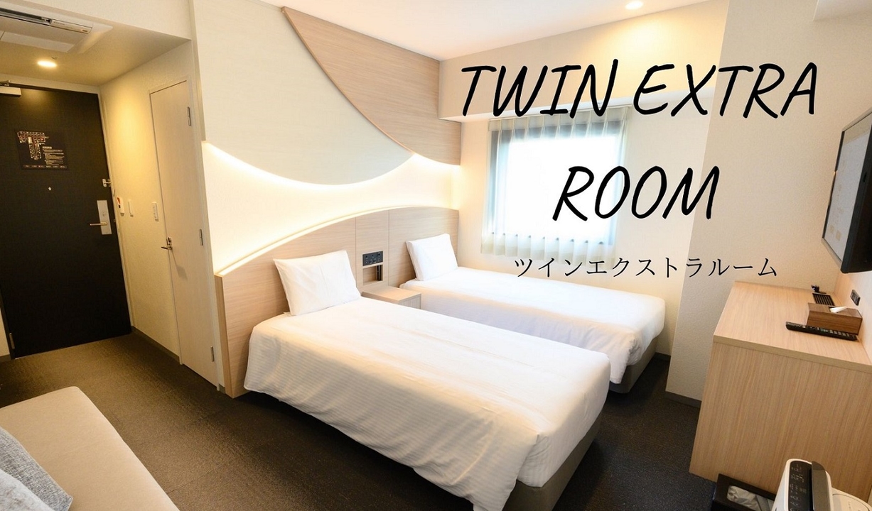 「TWIN EXTRA ROOM ツインエクストラルーム」の文字が入った客室の写真。白いベッドが2台並んでいる