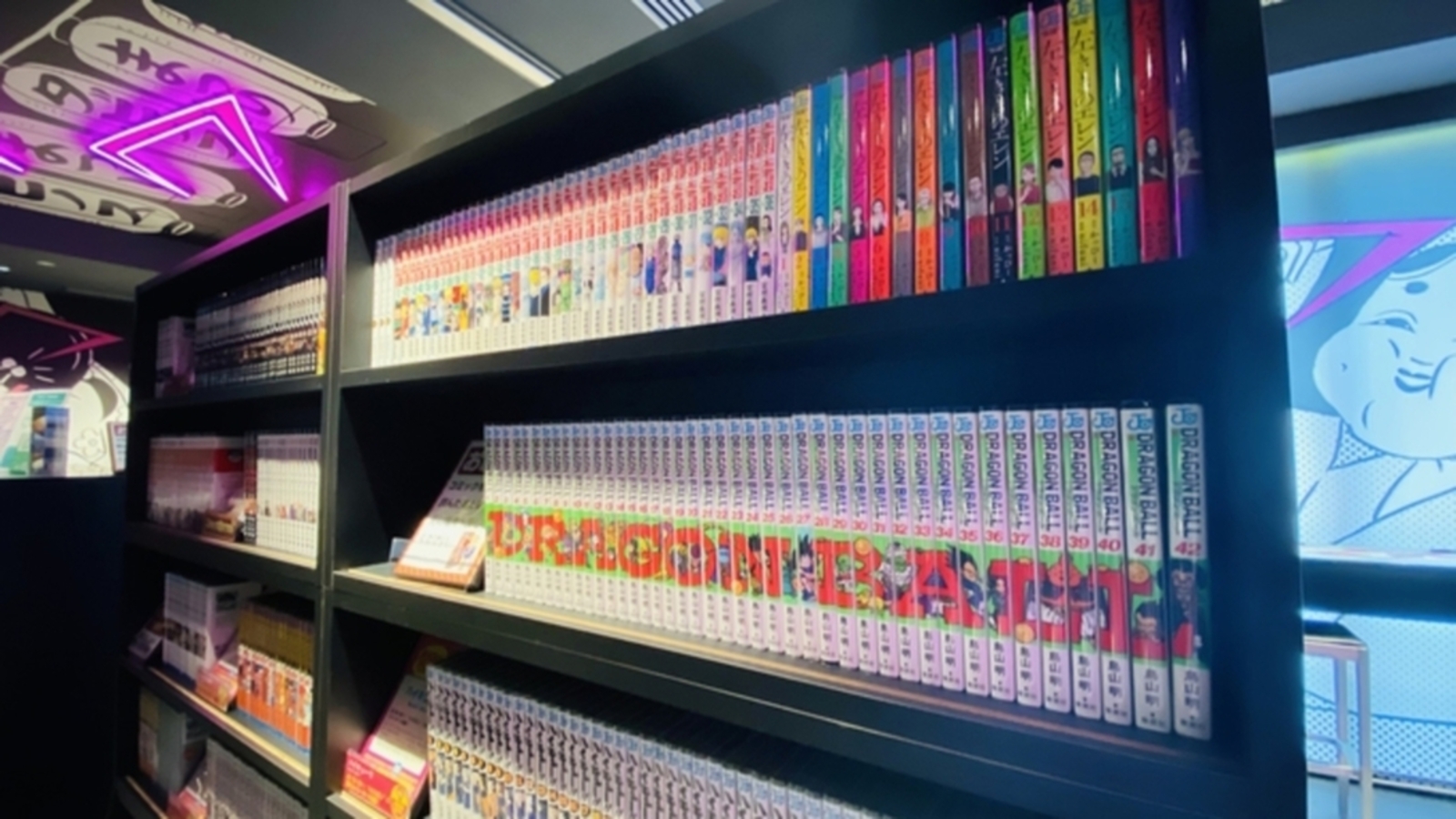 HOTEL TAVINOS Asakusaのラウンジの本棚。黒い棚にDRAGON BALLなどの単行本がずらりと並び、奥の壁にマンガの絵が描かれている