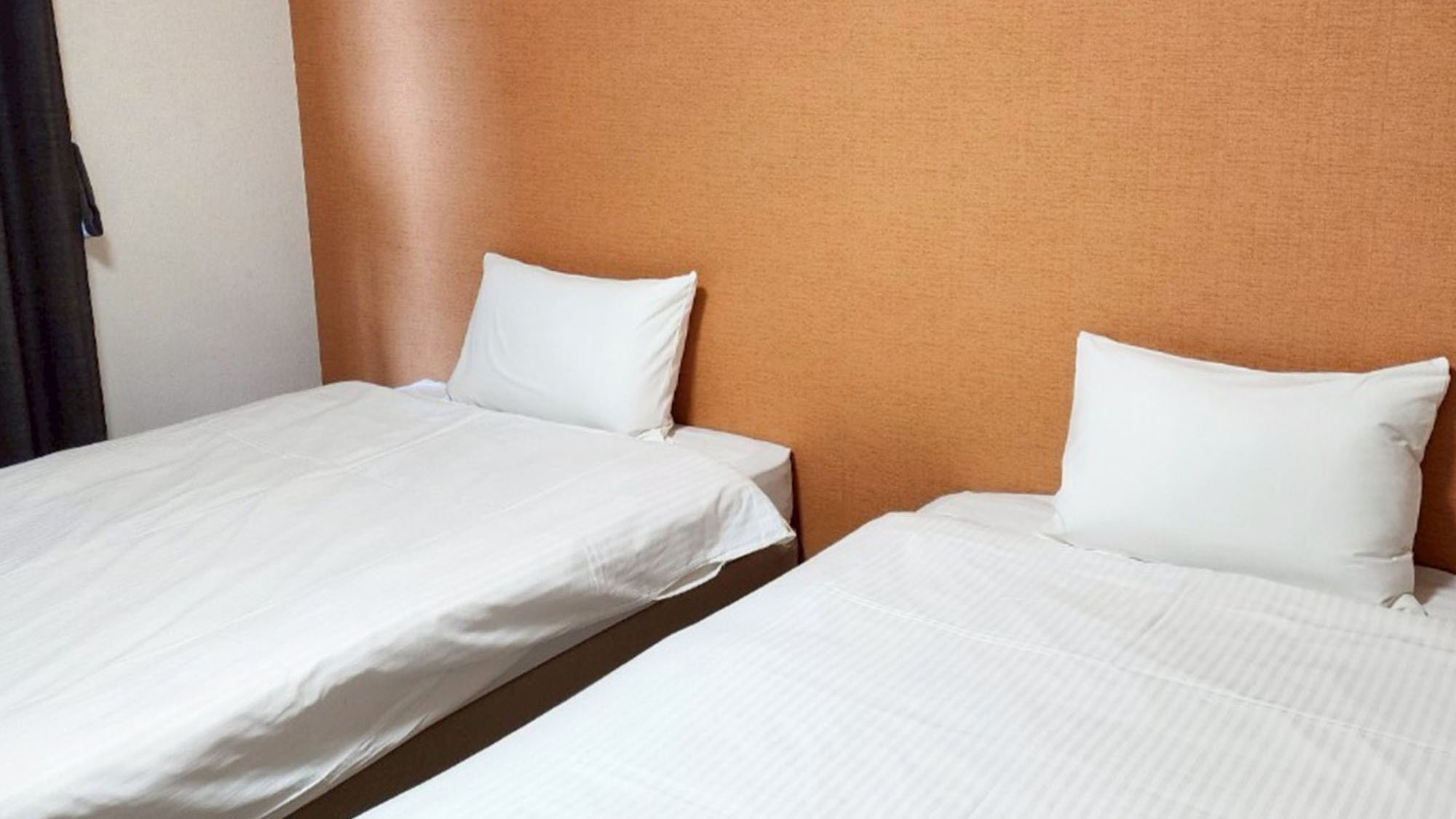 ・【702：寝室】シングルベッド2台を備えた1Kツインルーム。オレンジの壁が目をひきます