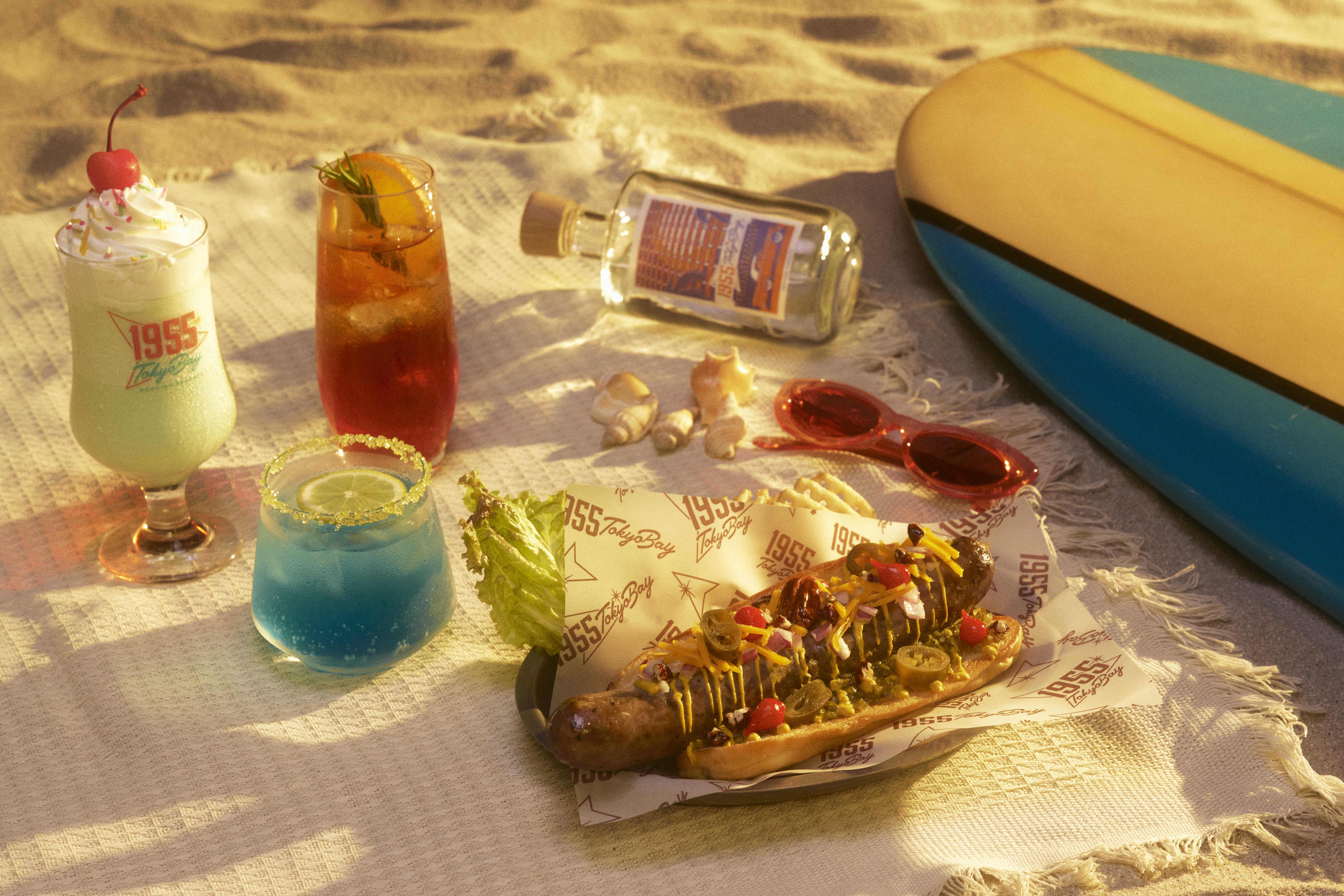 「Cafeteria」で期間限定のビーフホットドッグとドリンク3種を提供。「GIANT Beef Dog」は、ビーフを使ってアメリカンスタイルに仕上げたオリジナルソーセージが特徴。約200gのビーフソーセージはボリューム満点で、満足感のある一品。ドリンク3種は時間の流れとともに移り行くビーチサイドの風景をモチーフにしています。「サニーミントシェイク」は青空が広がるデイタイムを、「サンセットラムティー」は夕日に照らされるサンセットタイムを、「ムーン・マルガリータ」は月が輝くナイトタイムを表現しています。