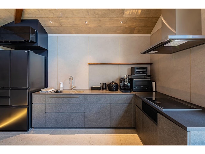 ダイニングテーブルの奥にはシックなIHコンロ付きのキッチン。調理家電や調理器具の揃ったキッチン...