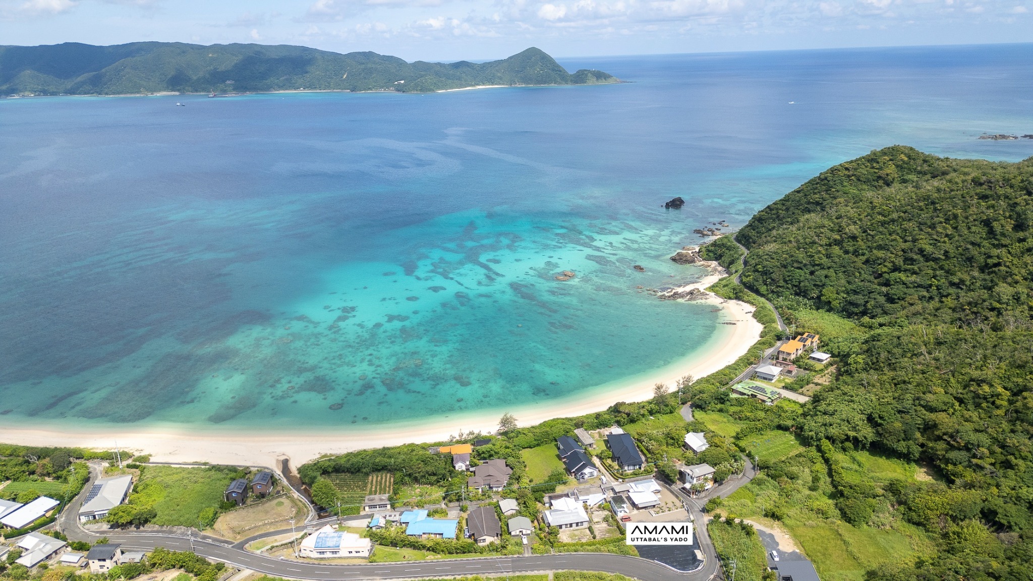 空から望む"うったばるビーチ"と集落。その美しい景色の中に"奄美うったばるの宿"は佇んでいます。