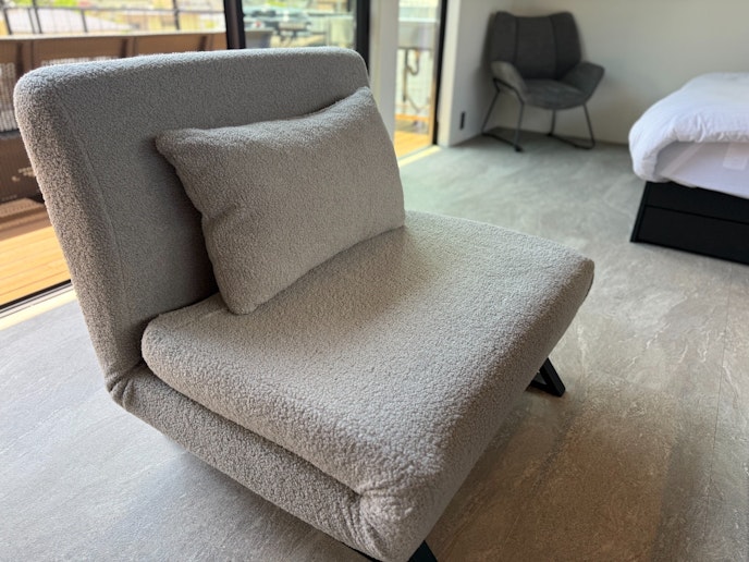 リビングルームの一部で、ゆったりとしたポーチチェアとソファが配置され、リラックスできる空間にな...