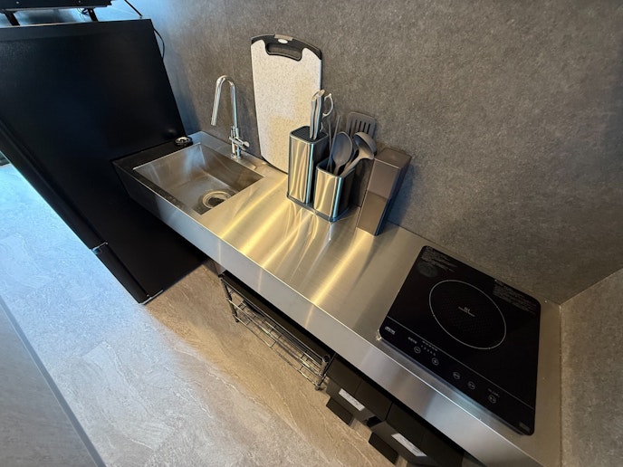 テンレス製のシンクと電気コンロが設置されており、シンプルかつスタイリッシュなデザインです。調理...