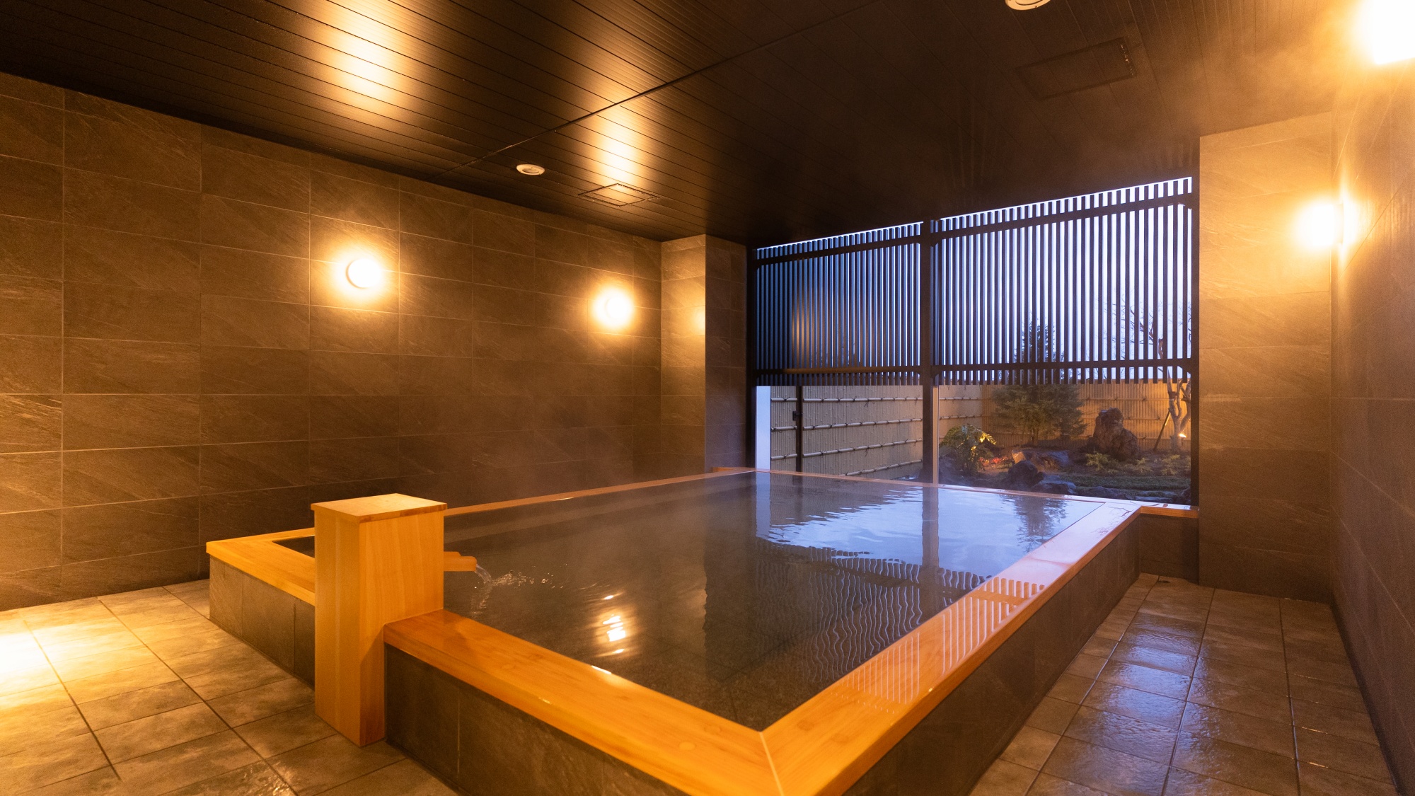 【温泉大浴場】庭園眺望の大浴場。雨や雪の日でもご利用いただける半露天仕様となっております。