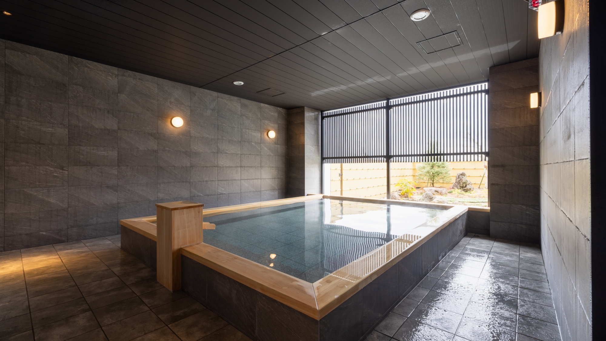 【温泉大浴場】庭園眺望の大浴場。雨や雪の日でもご利用いただける半露天仕様となっております。