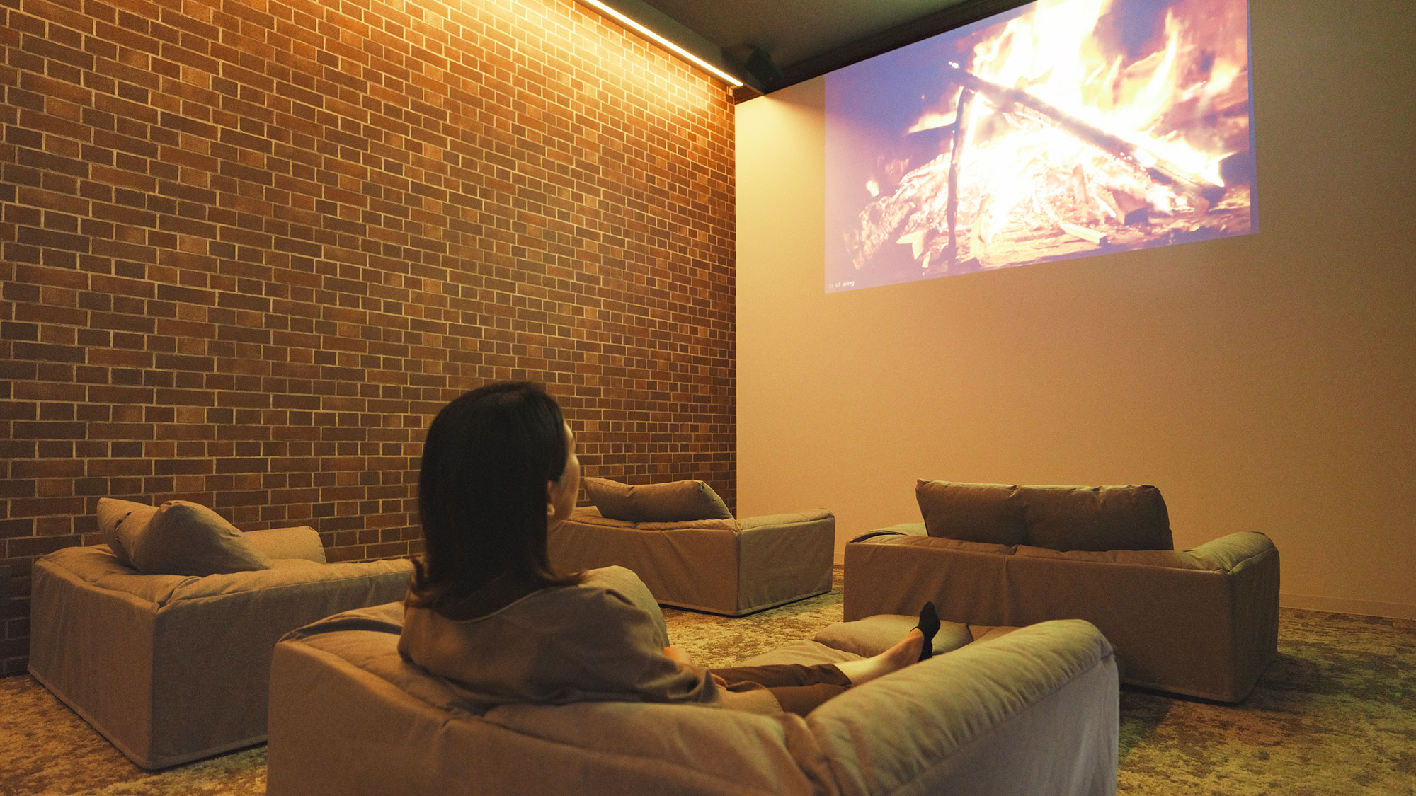 【最高の湯／ライブラリー】プロジェクターで焚火の映像を投影している寛ぎのソファースペース。