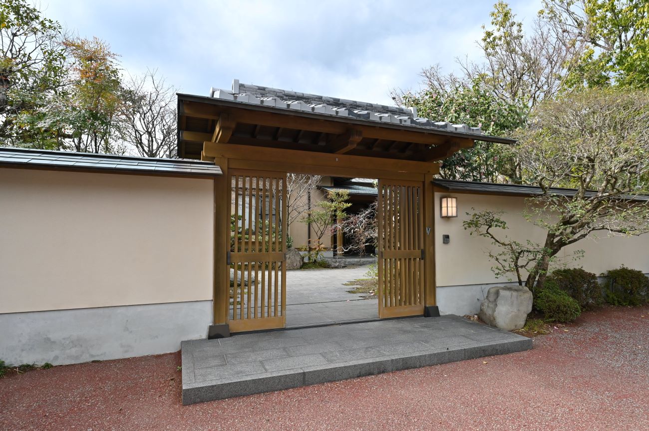 重厚な木の質感と石の落ち着きが調和した門は、和の趣きを感じさせながらも洗練された佇まい。お客様を特別な時間へと導きます。