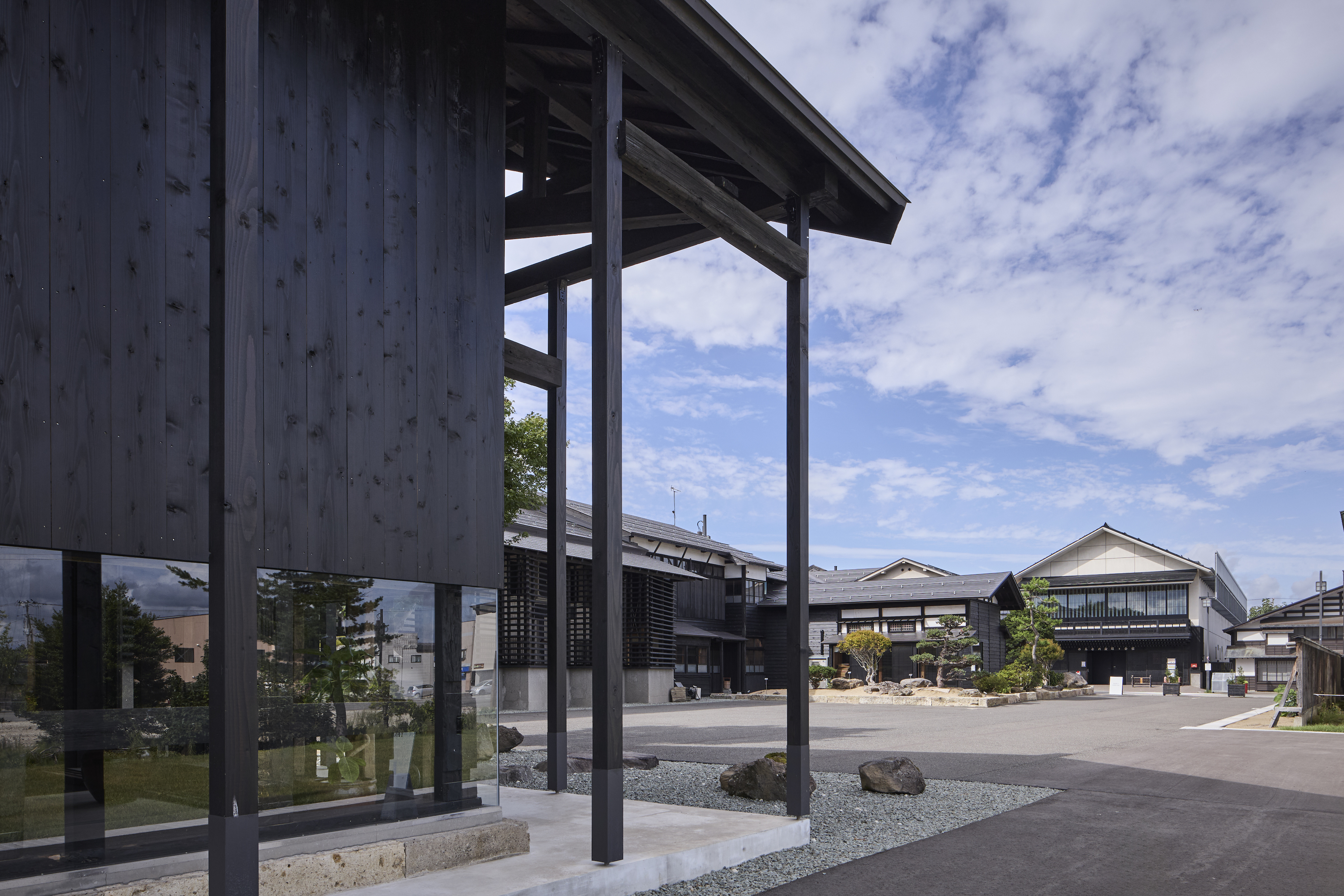 Facade｜米蔵を改修したラウンジ棟の奥に屋外ひろばと母屋を臨む