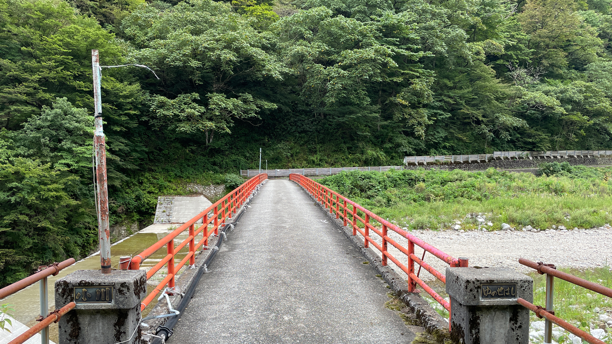 【天然洞窟露天風呂・蓮華の湯への道のり　赤い橋】看板の先には小川を渡る橋があります。