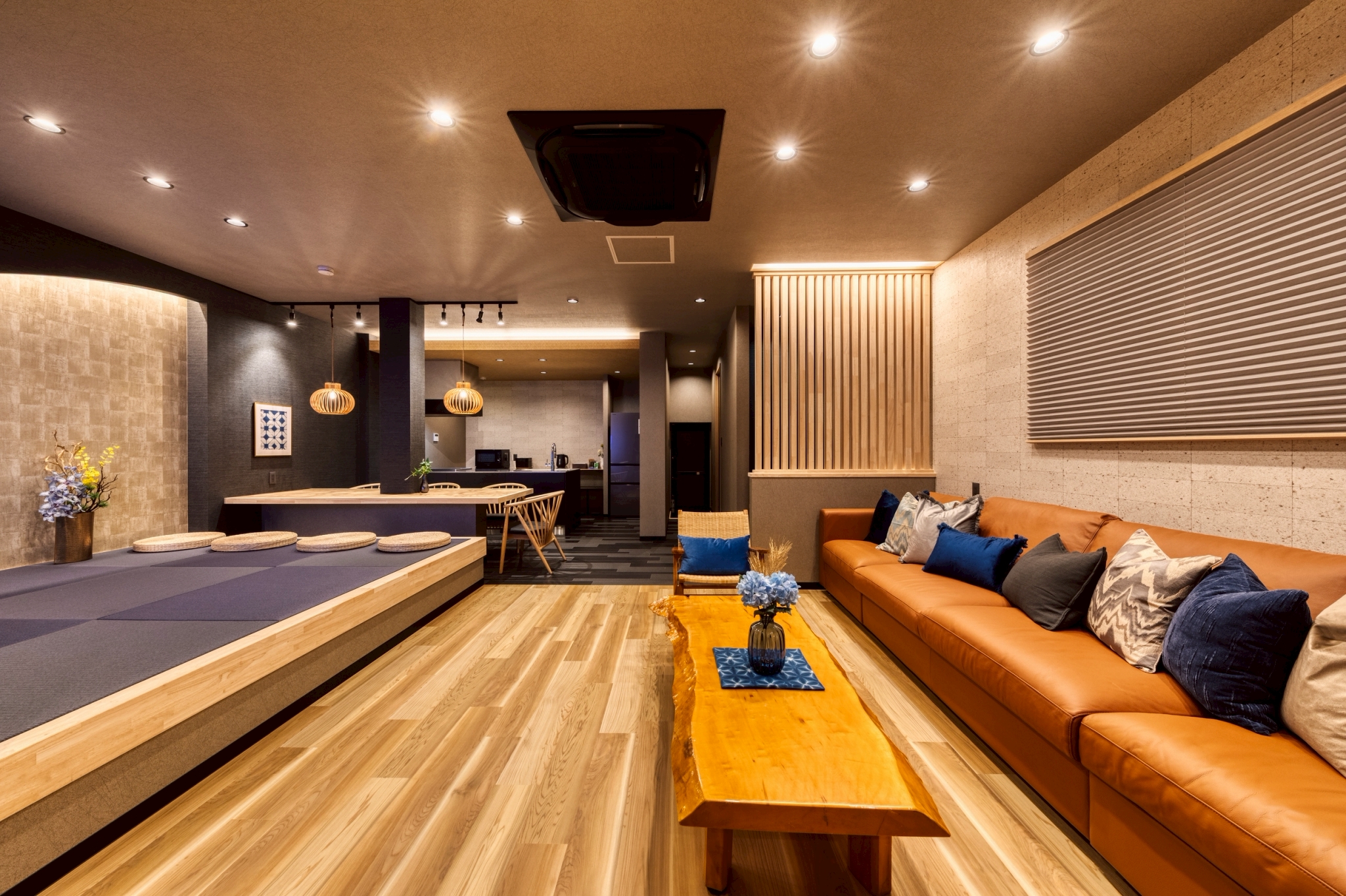 木の温もりとモダンなデザインが調和した広々としたリビングスペース。 大人数でもゆったりと寛げるロングソファと、自然素材を活かした無垢材テーブルが落ち着いた雰囲気を演出します。 畳を取り入れた小上がりスペースは、食事や談笑の場としてはもちろん、足を伸ばしてリラックスするのにも最適。