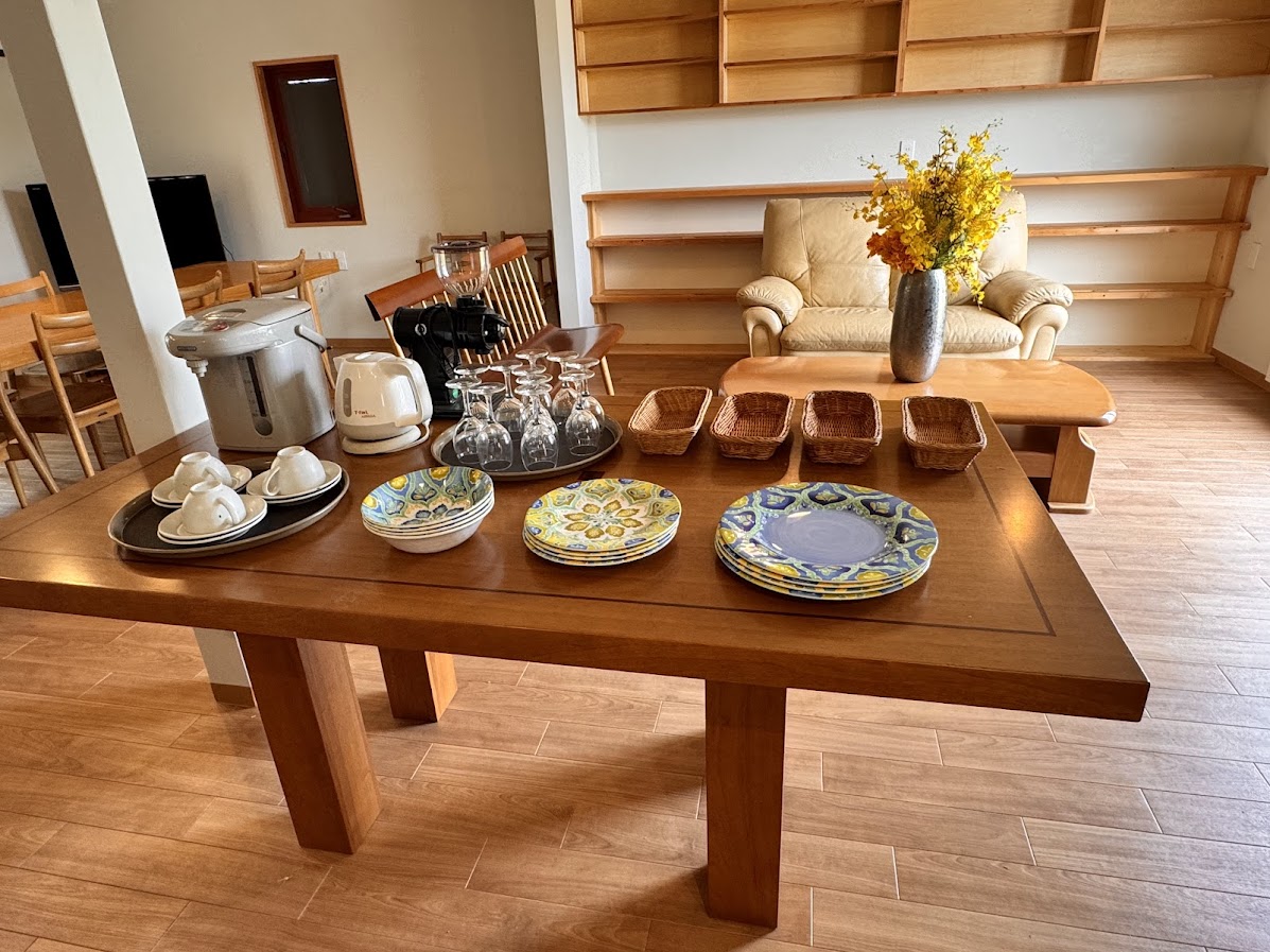 薫風舎の共有スペースには、滞在者が自由に使えるセルフカフェコーナーをご用意。湯沸かしポットやコーヒーメーカー、炊飯器などの家電に加え、カップやプレート、カトラリーも完備。朝の一杯から軽食の準備まで、気ままに過ごせる設備が整っています。木の温もりに包まれた空間で、旅の合間のひとときをどうぞ。