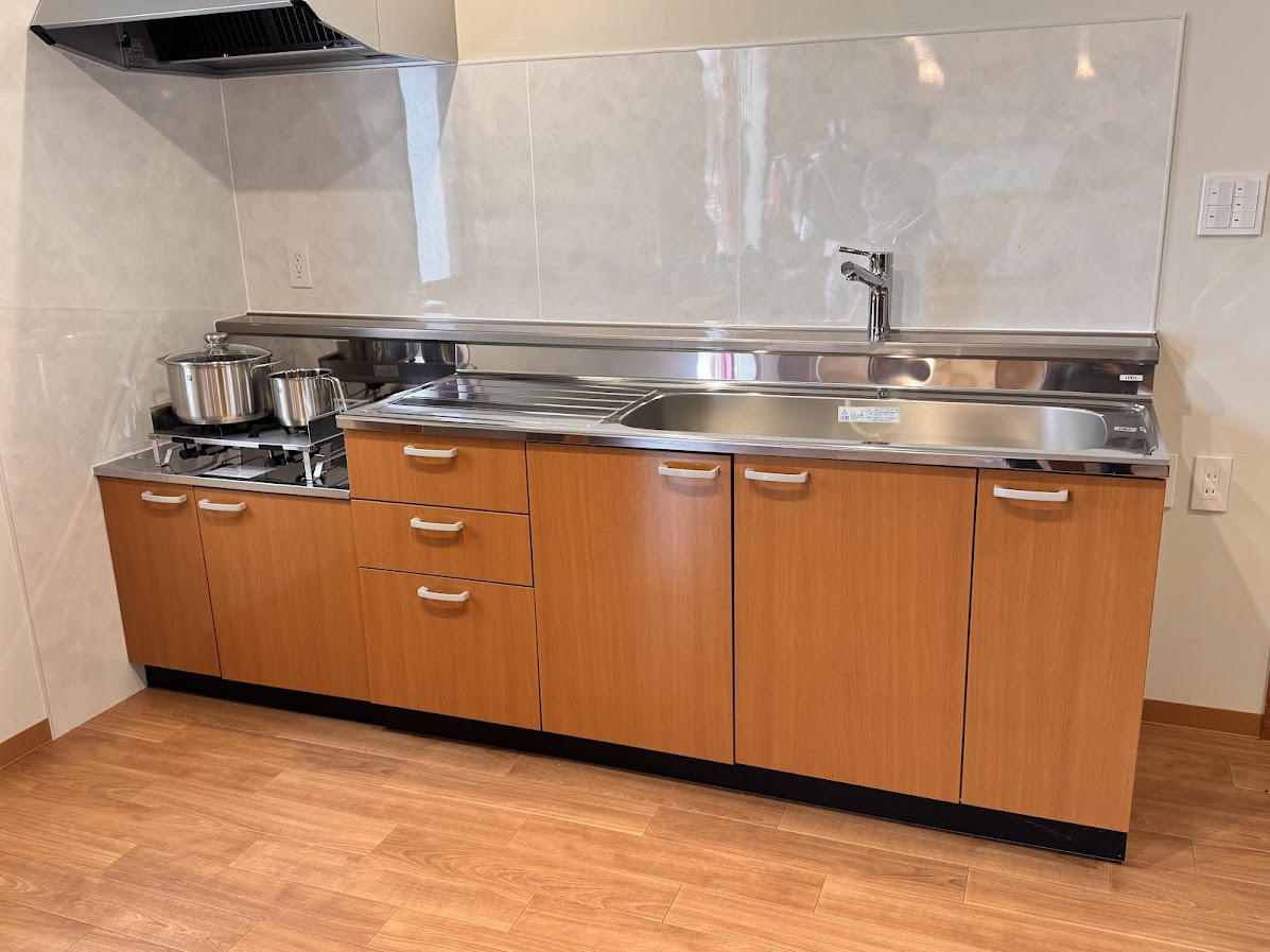 ステンレスの調理台と木目の収納が調和する、薫風舎の専用キッチン。コンロやレンジフード、シンクなど基本設備が整っており、滞在中の自炊にも対応可能です。鍋を火にかける音、湯気の立ちのぼる瞬間&mdash;&mdash;旅先でも、日常の味を再現できる安心の空間です。