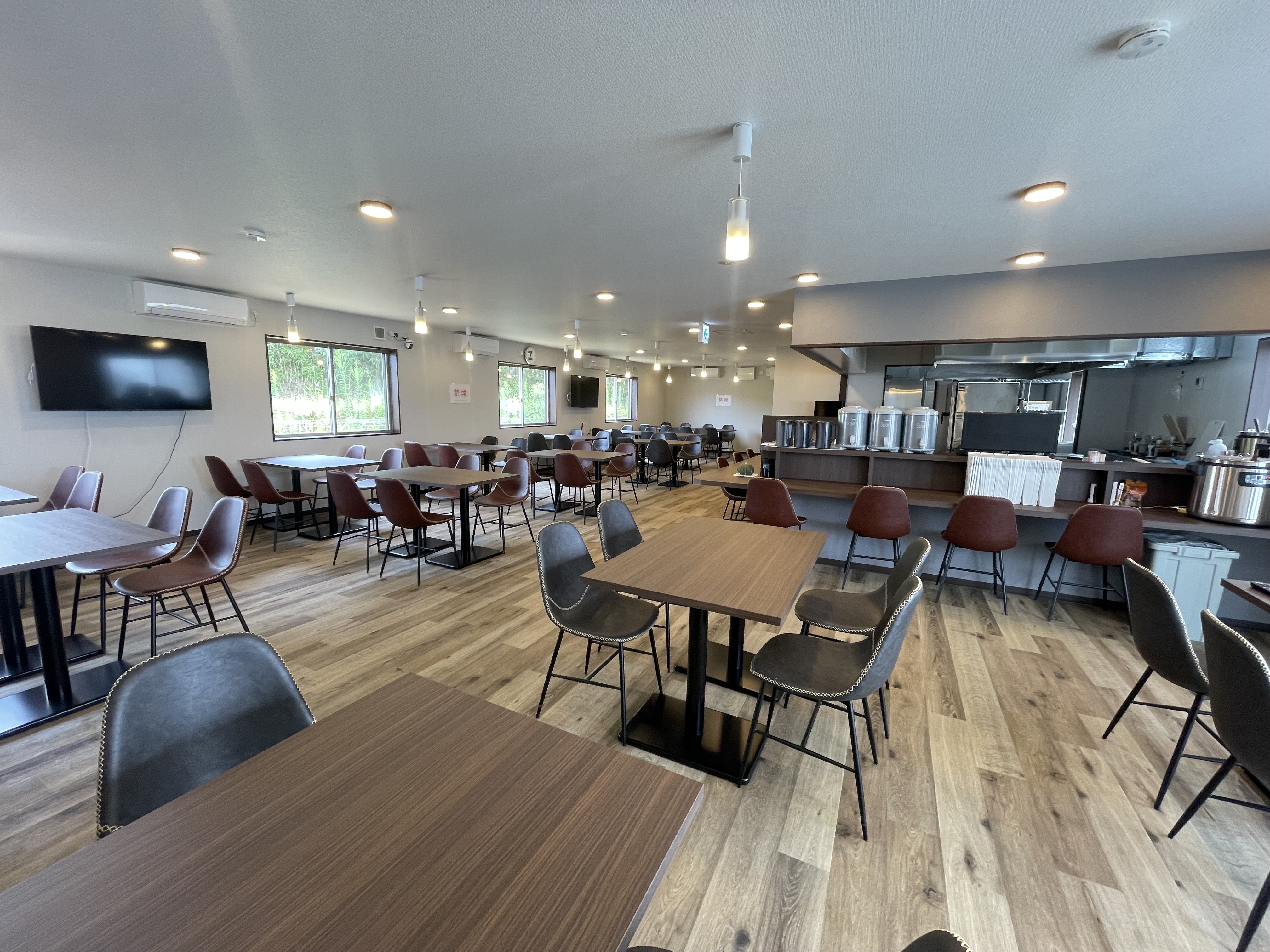 木目調で落ち着く新築ダイニング。自然光が差し込む開放的な空間で、朝食・夕食をゆったりお楽しみいただけます（提供内容は日程により変わります）。団体利用や長期滞在の食事拠点にも便利です。