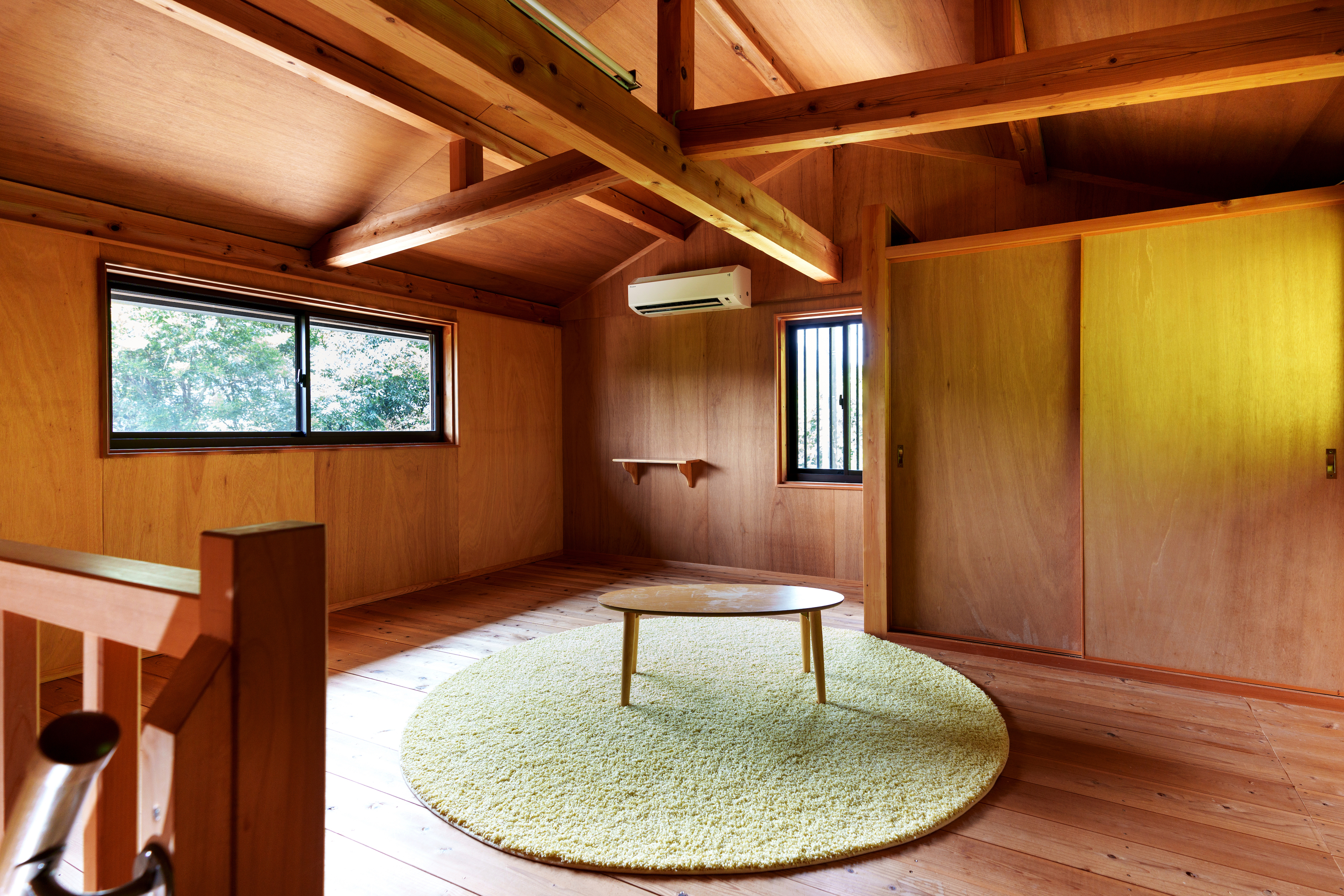 梁と天井、床まで、木の表情がやさしく連なる二階の空間。 窓から差し込む緑の気配が、時間の流れをゆるやかにほどいていく。 円形のラグと低いテーブルが、何もしない贅沢を受け止める場所。 読書も、昼寝も、ただ考えるだけの時間も―― 滞在の&ldquo;余白&rdquo;が、ここで深呼吸を始める。