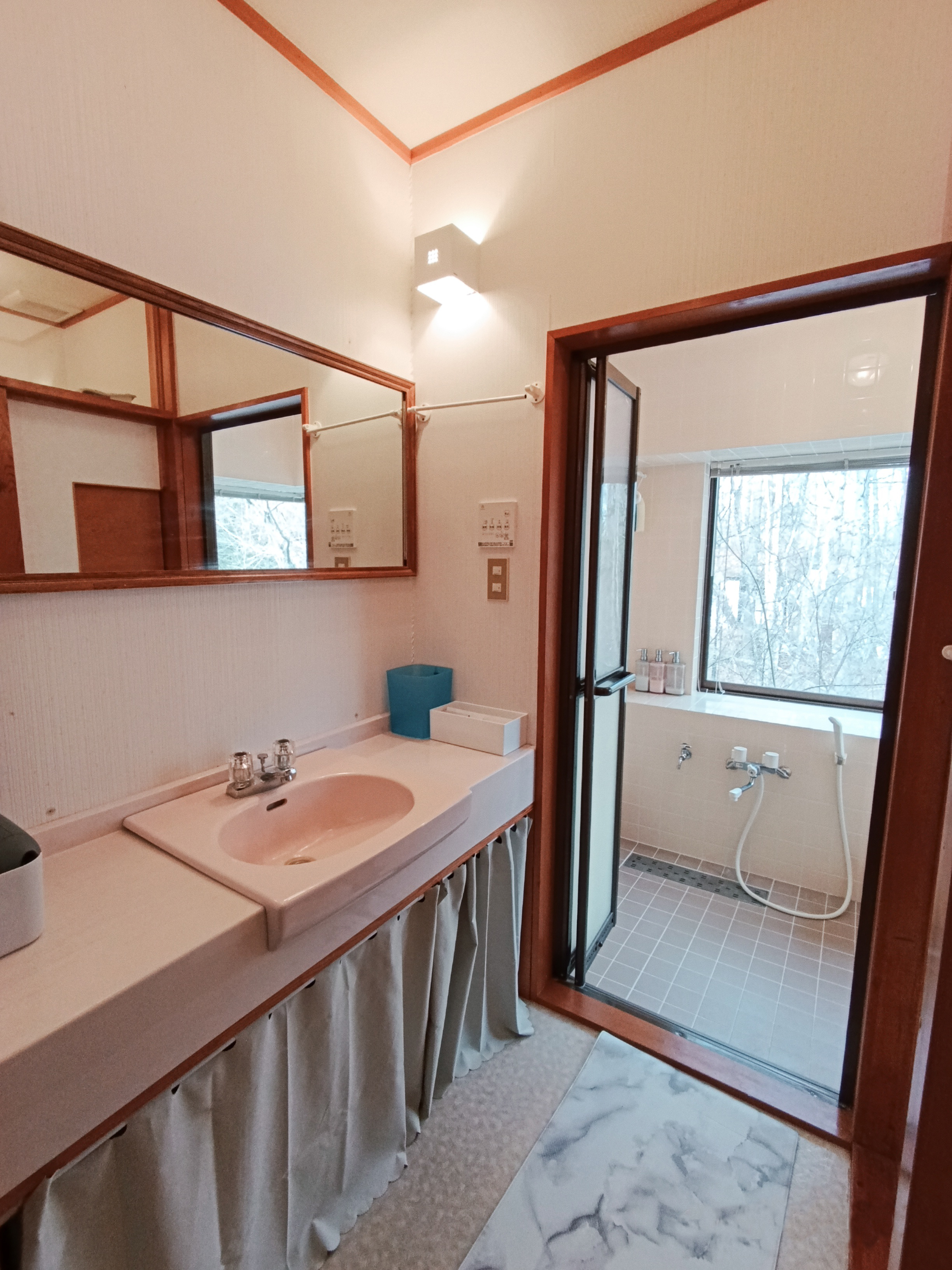 Clean and functional bathroom with a separate wash area and bathtub. Enjoy a relaxing bath with a peaceful forest view through the window.