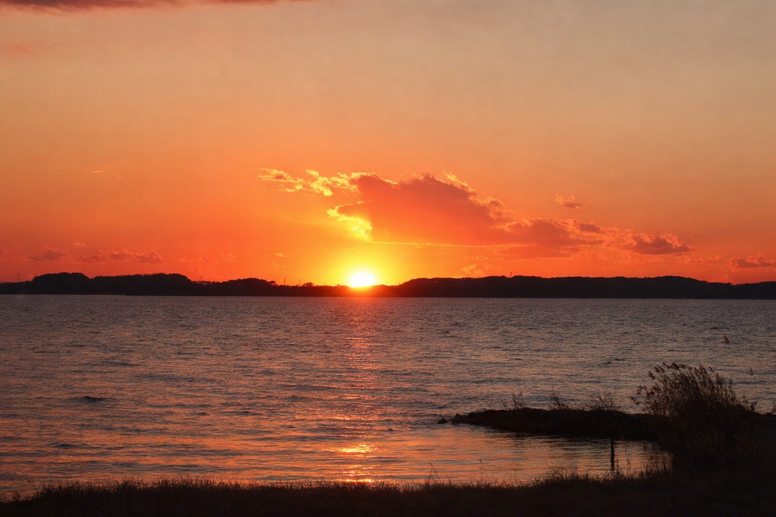 湖面に沈む夕日が空と水面をオレンジ色に染める、静かで幻想的なひとときを切り取った空間