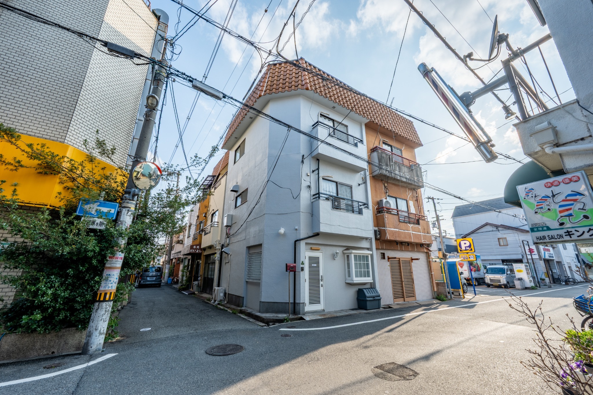 角の白い壁の建物が当施設です。建物のすぐとなりが駐車場です。