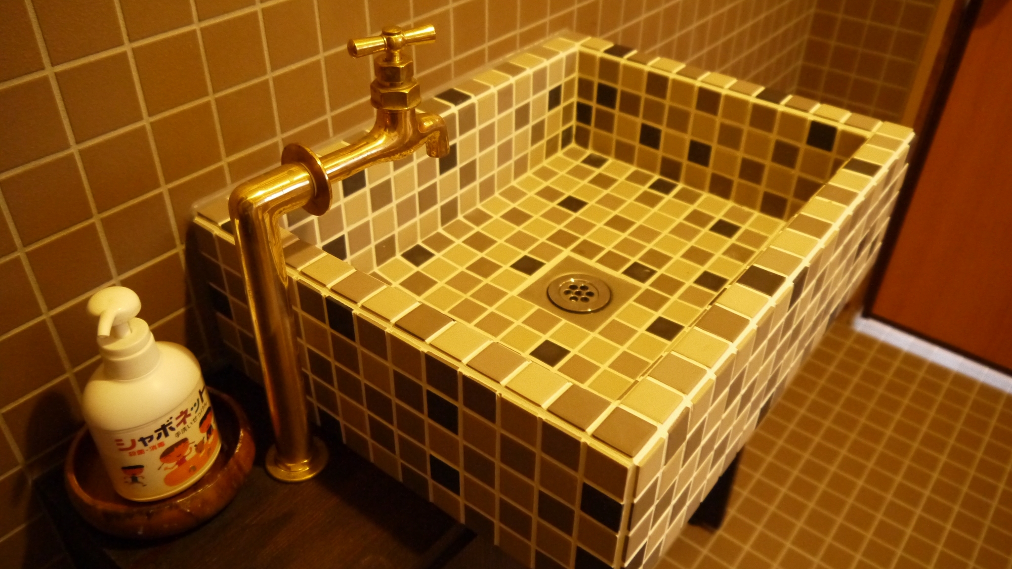 *明るいカラータイルとちょっとレトロな水栓が印象的な共同トイレのお手洗い。