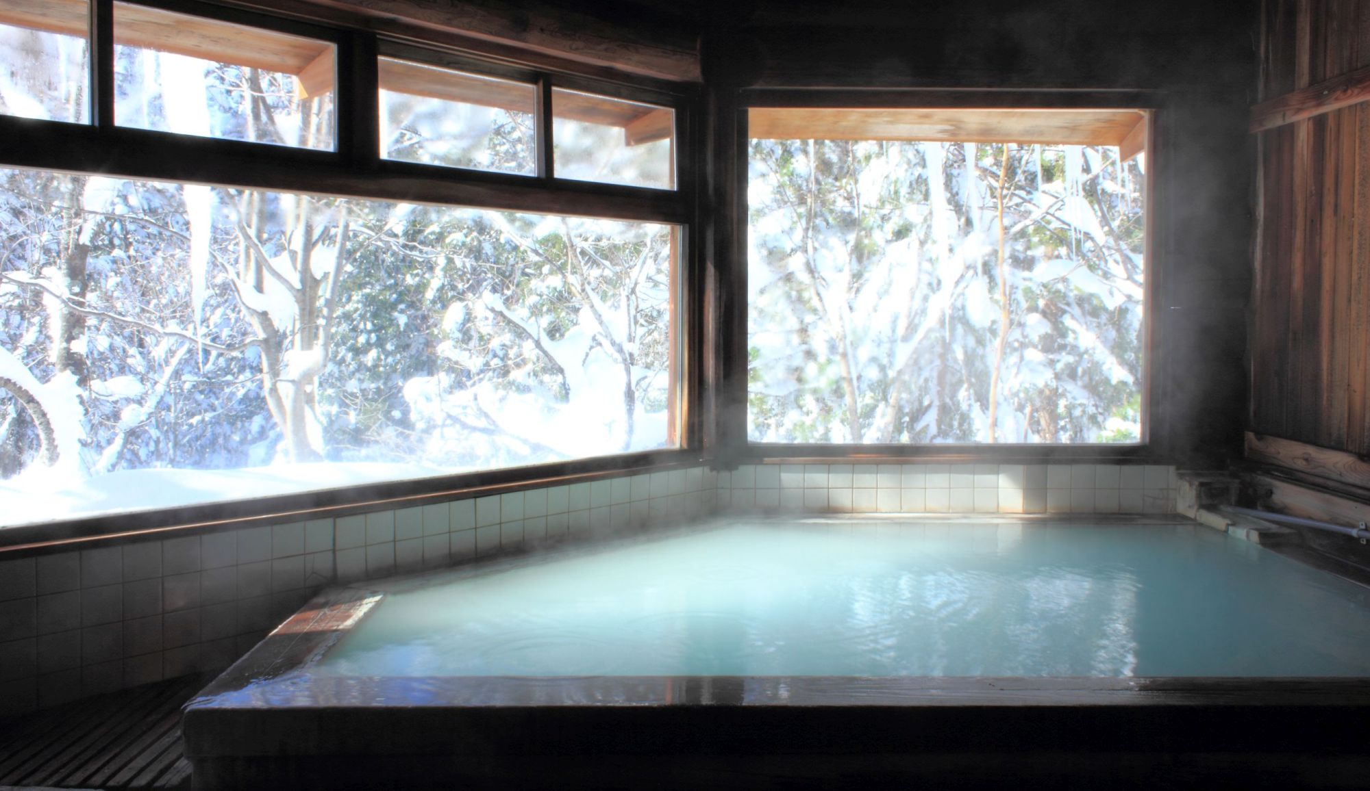 【丸太造りの天然温泉】スキーで疲れた後は雪見風呂でほっこりと。広めの窓から雪景色が眺められる