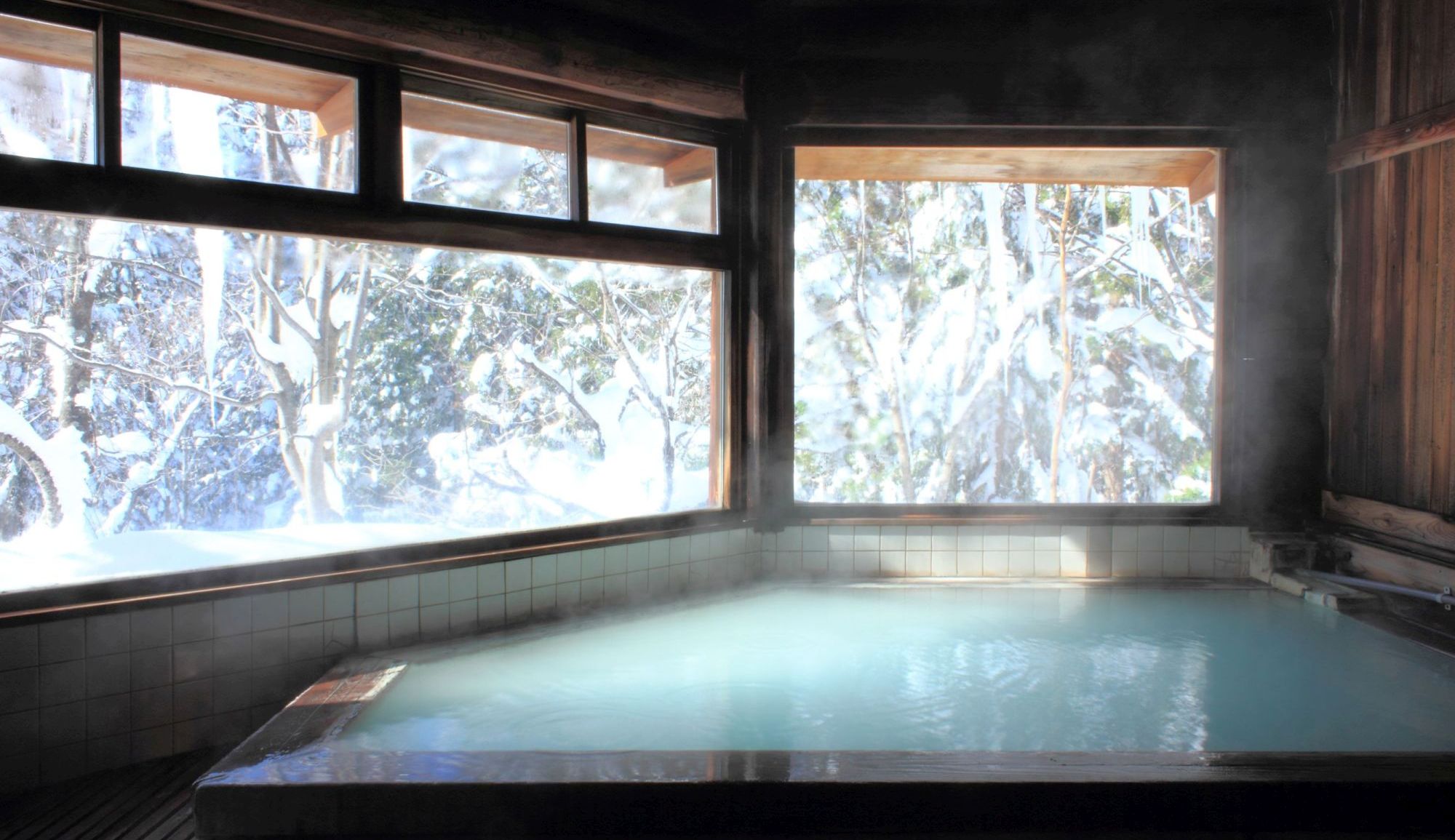 【丸太造りの天然温泉】スキーで疲れた後は雪見風呂でほっこりと。広めの窓から雪景色が眺められる