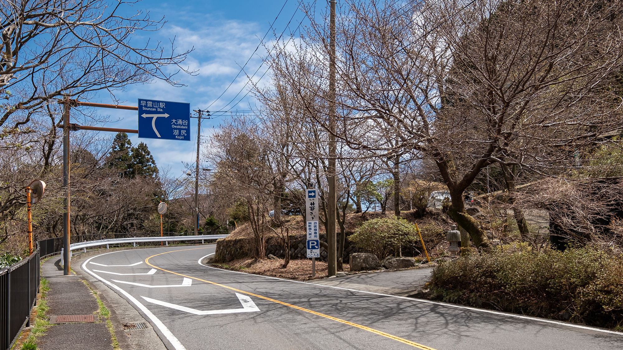 【駐車場のご案内】大きく右カーブする手前の青い標識、すぐ手前右手に駐車場入口がございます。