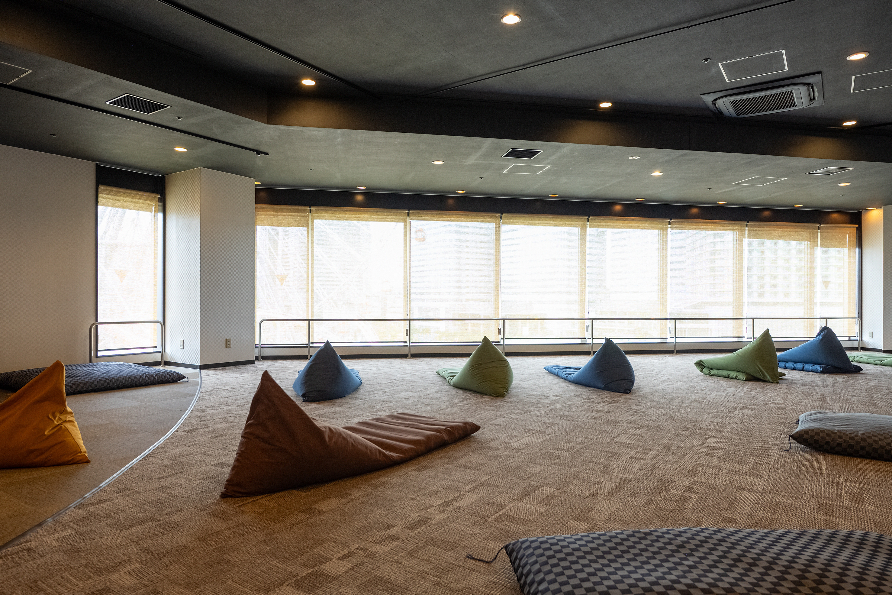 横浜みなとみらい 万葉倶楽部のくつろぎコーナー。カーペットの広い部屋にビーズクッションが置かれ、窓が横に並んでいる