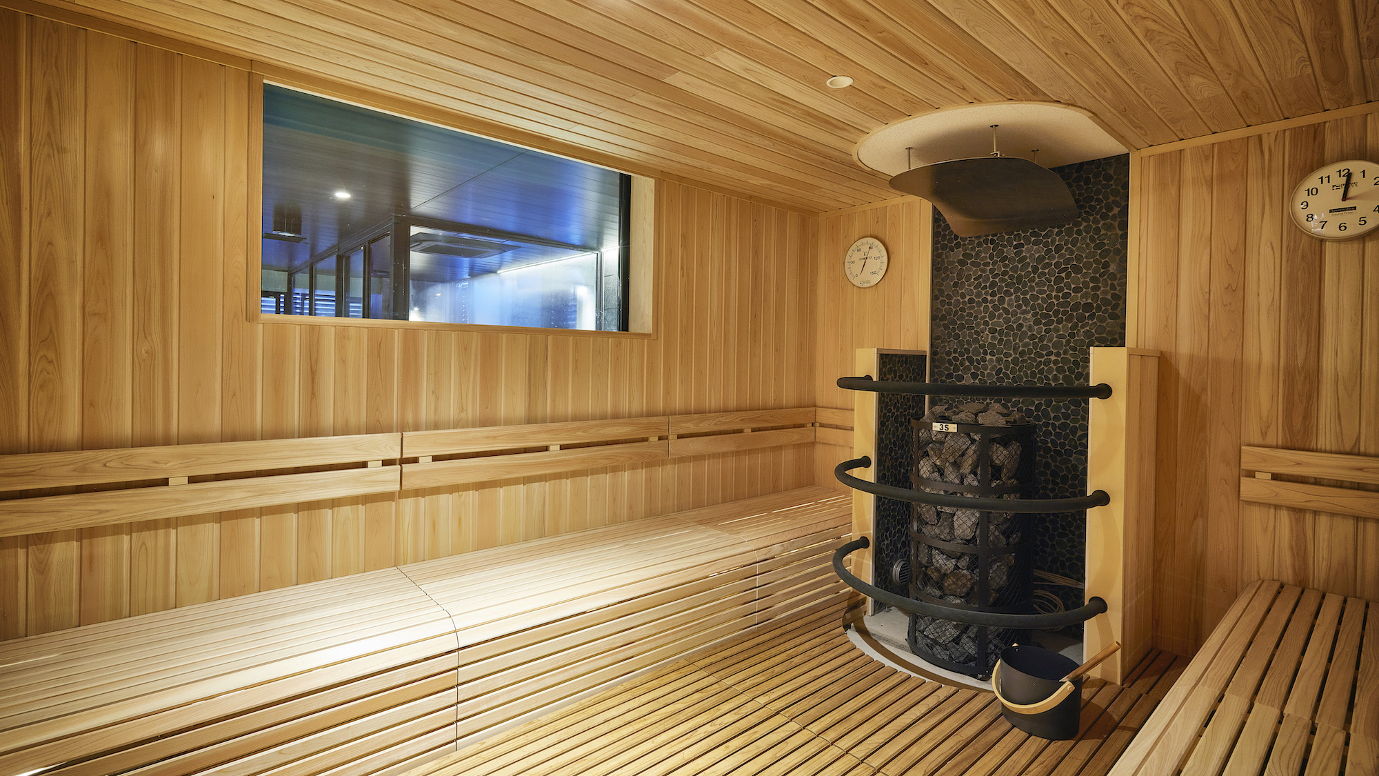 3S HOTEL ATSUGIのフィンランド式サウナ。木のベンチと、石を積んだサウナストーブ