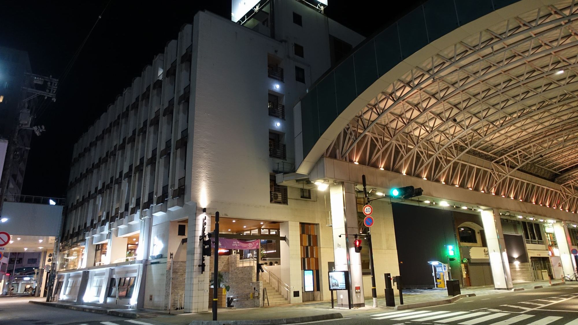 夜の街に映えるホテル外観。アーケード直結の便利な立地で、急な雨でも安心です。ホテル入り口は開放感があり、お仕事や観光帰りのお客様を温かな光でお迎えいたします。