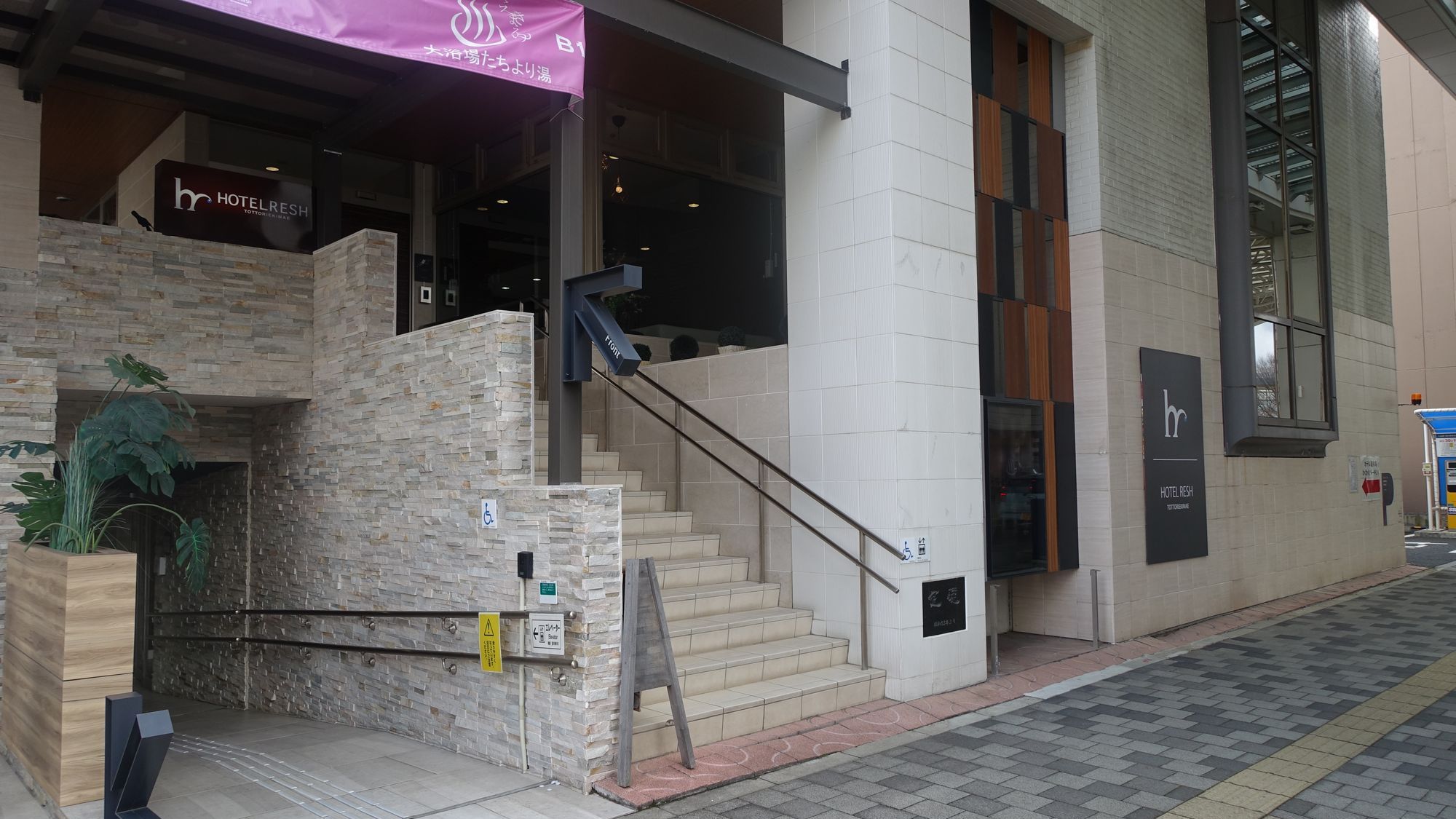 写真左側のスロープを進むとエレベーターがございます。ロビー・フロントへ階段を通らずにアクセスできるため、どなた様も安心してご来館いただけます。