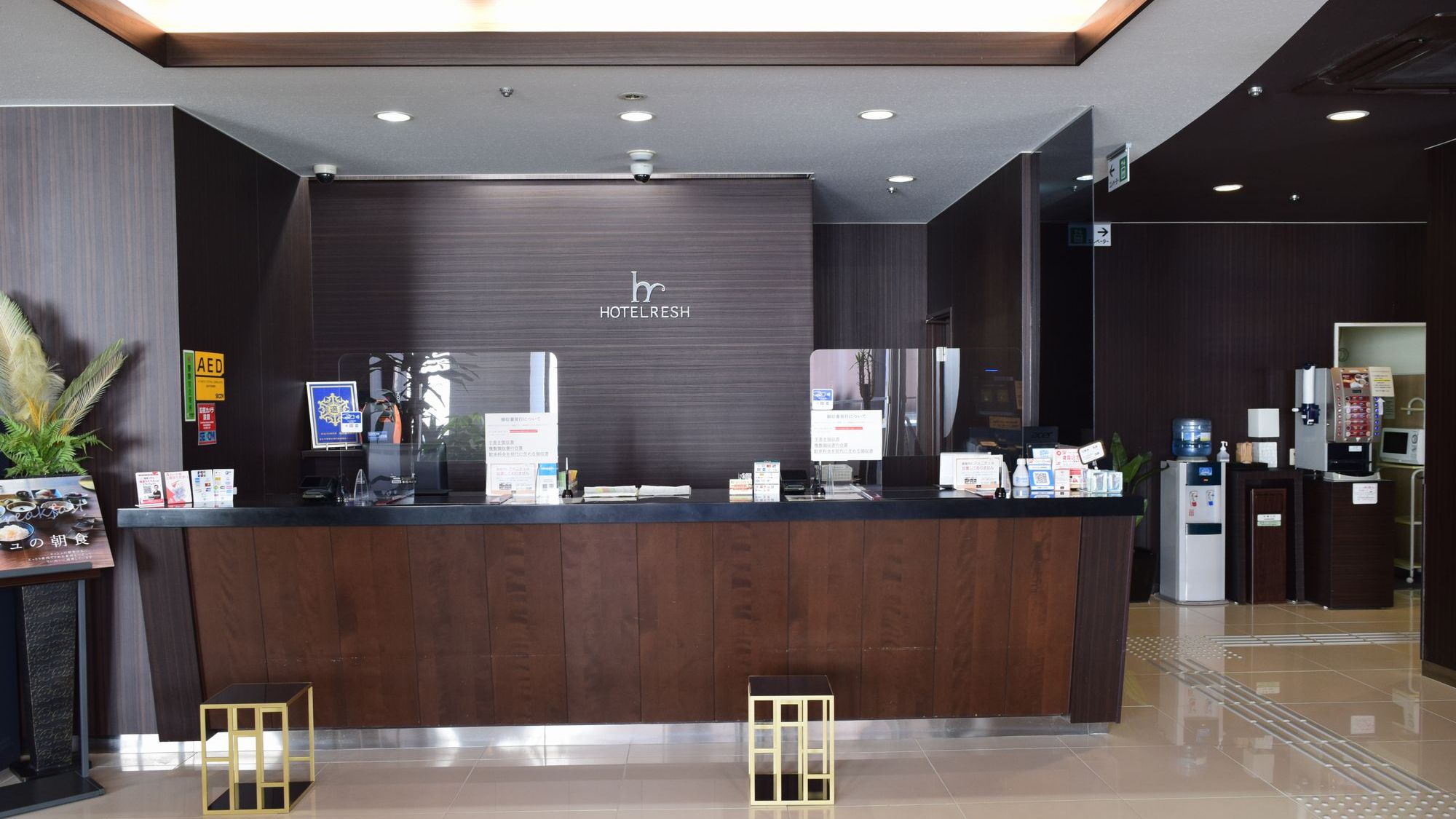 HOTEL RESH 鳥取駅前のフロントデスク。ダークブラウンを基調とした上質な空間で、皆様をお迎えいたします。ロビー内にはAEDやフリードリンク設備も完備しており、安心・快適なご滞在をお約束いたします。