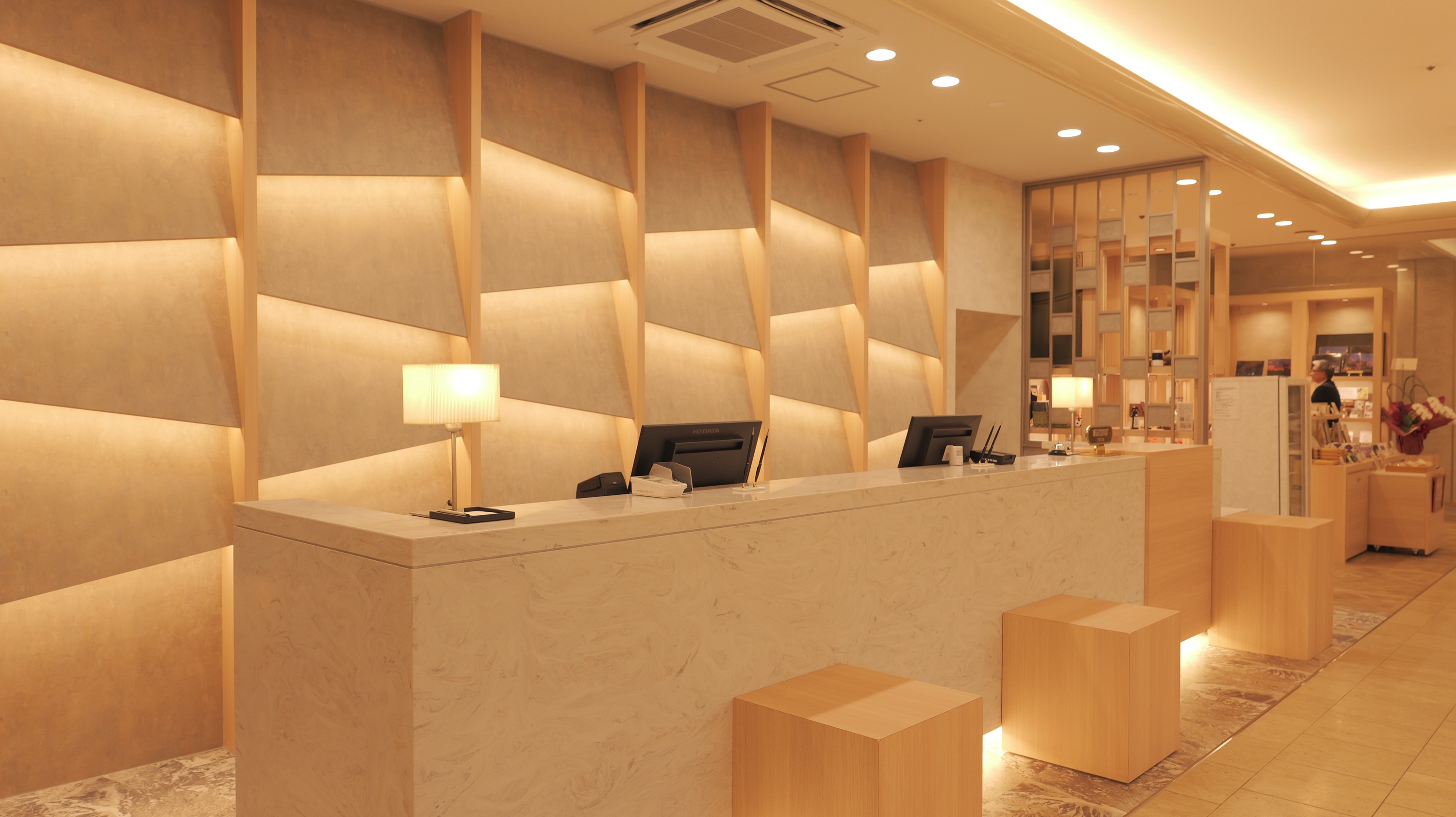 カウンターバックには、城下町の面影が残る城東地区の建物の屋根瓦をモチーフに間接照明も合わせてデザインしており、明るくお客様をお迎えできるフロントにしております。フロント廻りにはウエルカムラウンジを新設しており、津山の新しい発見や出会いが生まれるスペースです。また、ショップ(売店)もリニューアルし、取り扱い商品も増え、多くの津山プロダクトを触れれるように致しました。