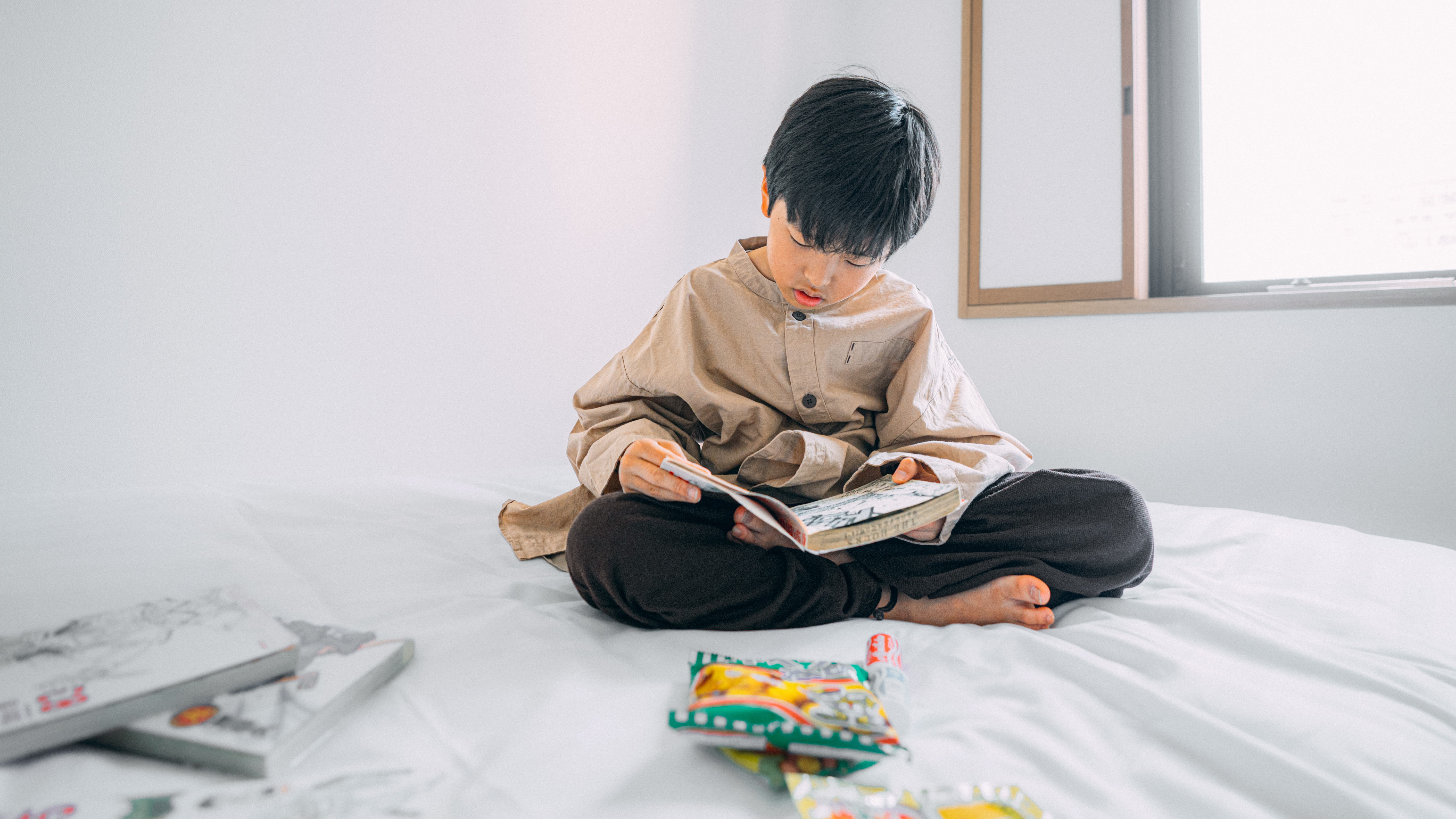 3S HOTEL HIRATSUKAの客室。白いベッドの上で、子どもがあぐらをかいて漫画を読んでいる