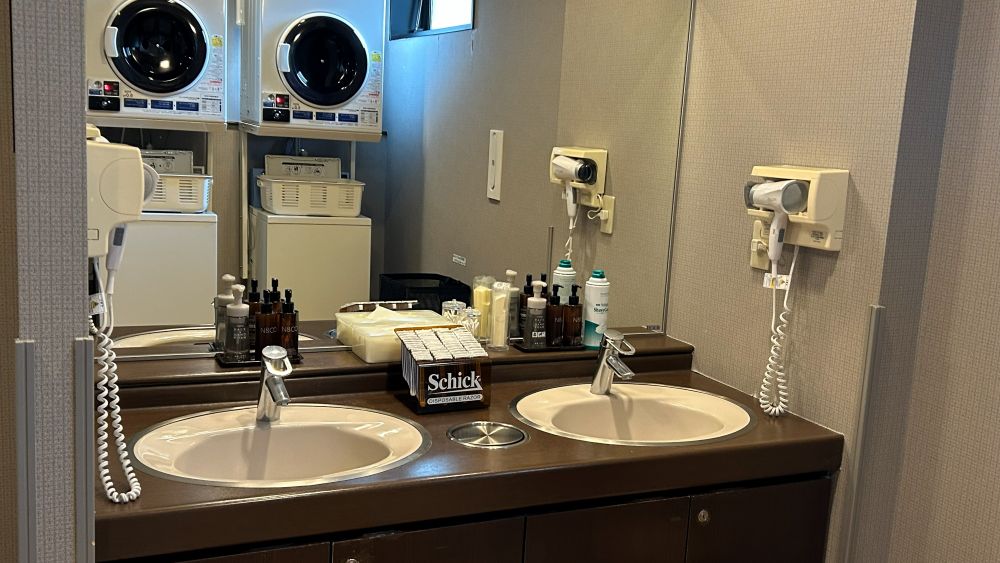 【男性大浴場脱衣所②】洗面スペースでございます。お風呂上りのケアに必要な化粧水も取り揃えております。