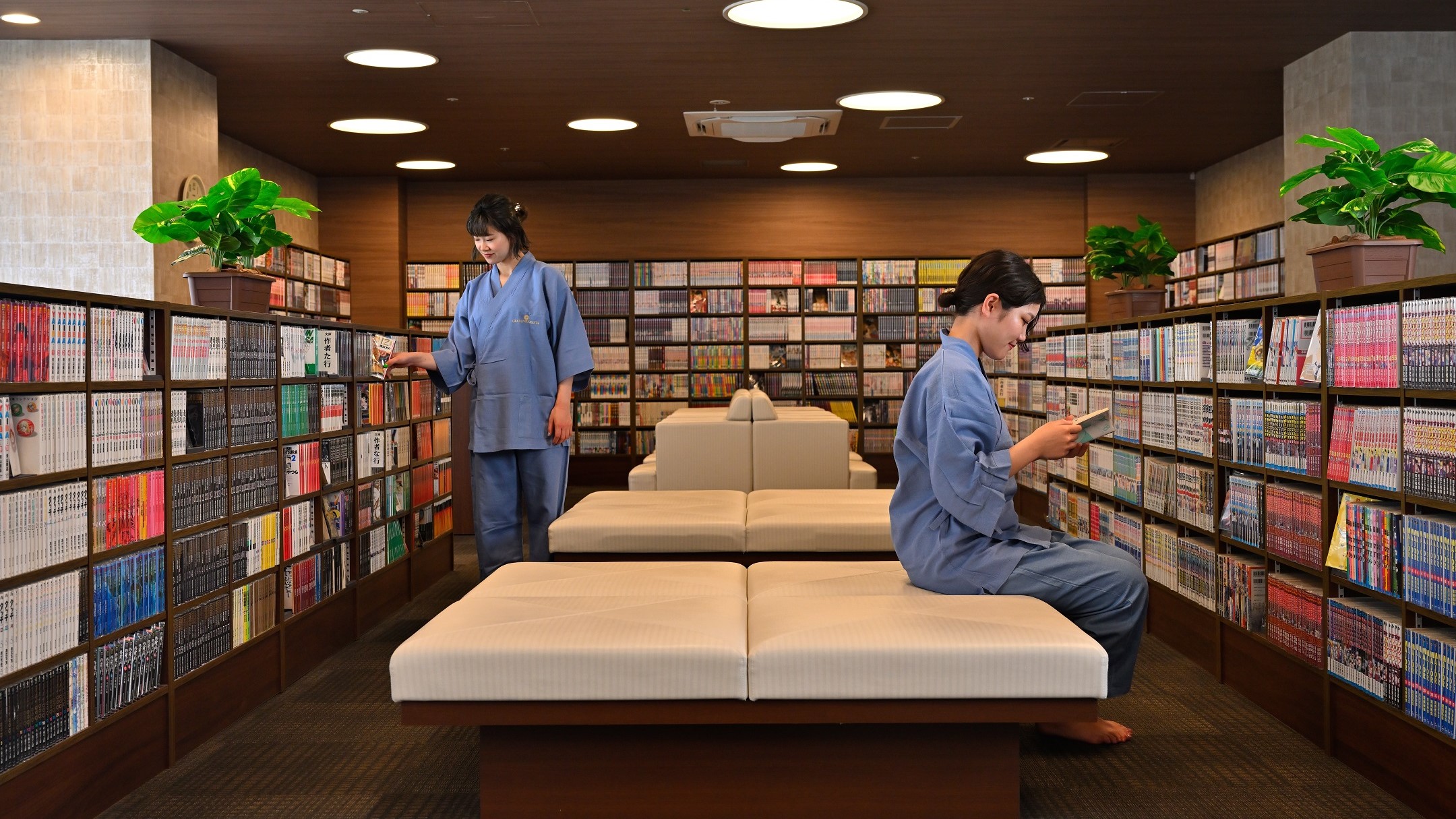 華楽の湯のコミックコーナー。壁際と中央の本棚に漫画が並び、館内着の人がソファで読んでいる