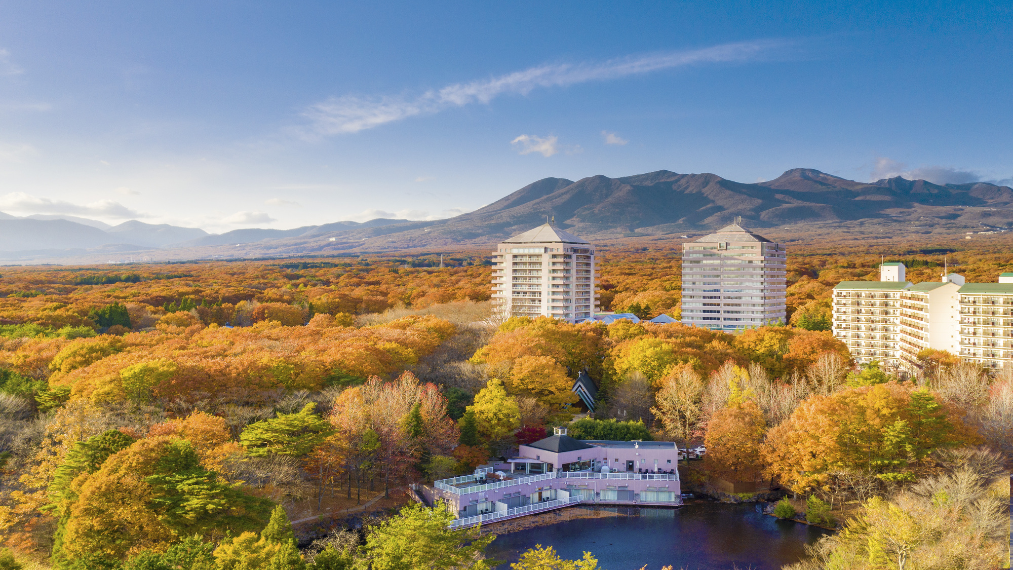 紅葉の森に囲まれたホテルエピナール那須の外観と、うしろの山並み