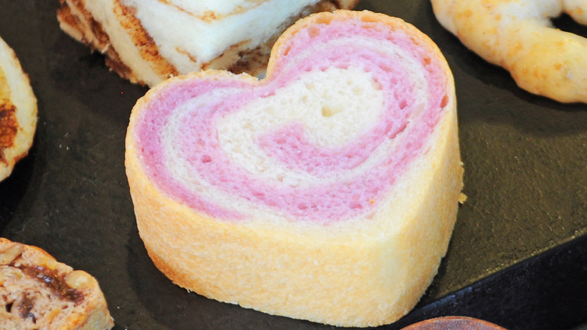 【パンメニューの一例】沖縄県特産紅イモのパン生地にミルククリームを巻き込んだ『ハートブレッド』