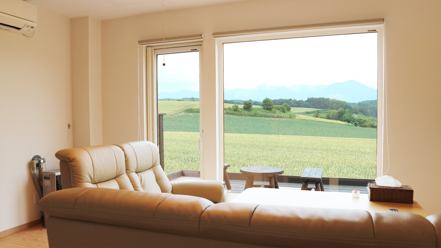 *プライベートハウス／リビングのソファに腰かけ、大きな窓の外に広がる富良野の絶景を堪能できます。 