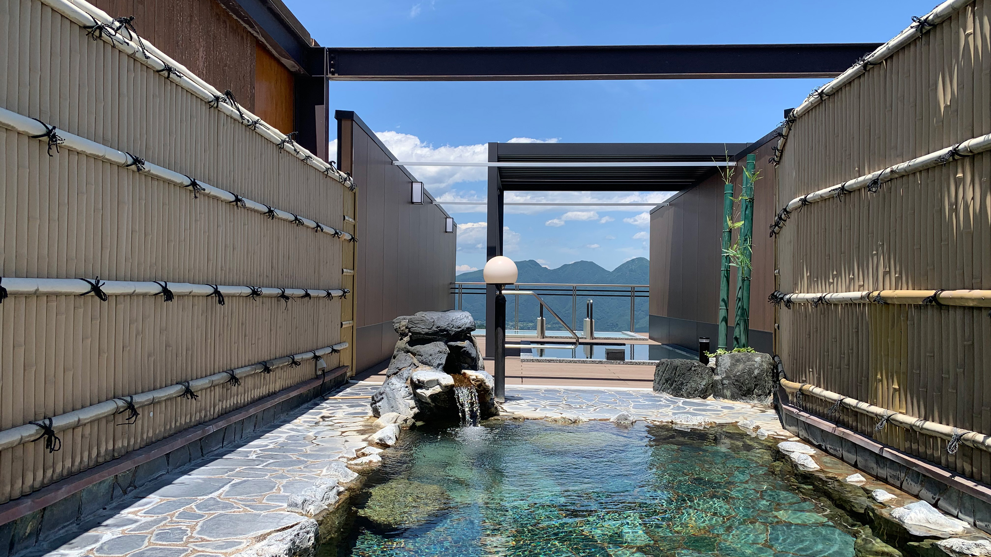 とどろきの8階の展望露天風呂。竹垣に囲まれた岩風呂の先に、山並みと青空が見える
