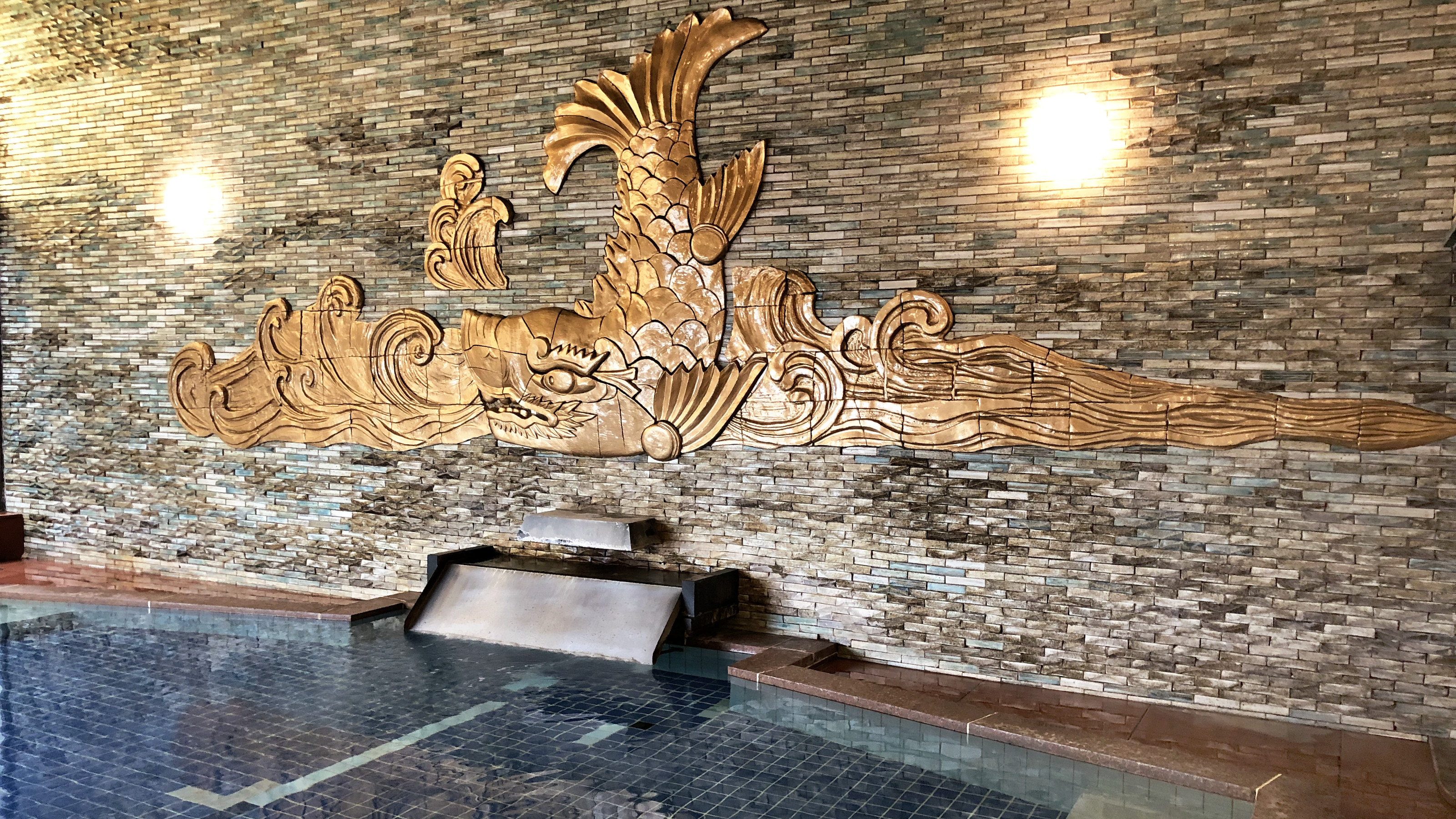 熱海 金城館の大浴場。岩壁に金色の彫刻がほどこされた広い湯船